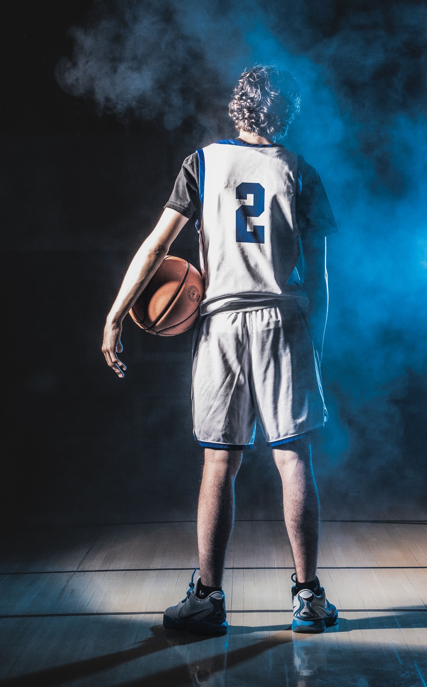 Player in white uniform number 2 stands on basketball court with blue smoke effects.