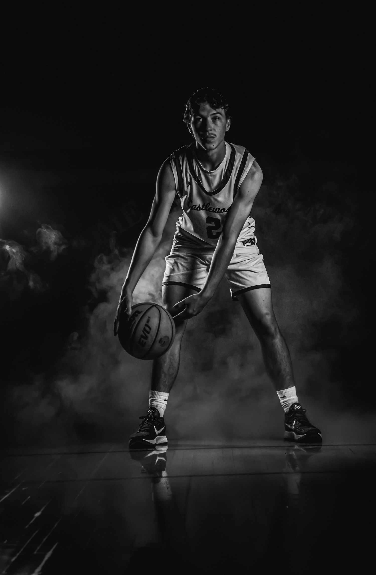 Black and white image of basketball player in defensive crouch with smoky atmosphere.