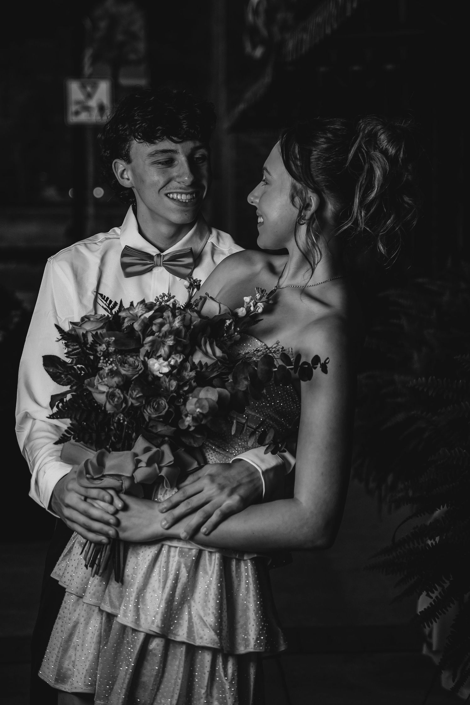 Black and white photo of a couple sharing a romantic moment while holding a beautiful floral bouquet at a formal event.
