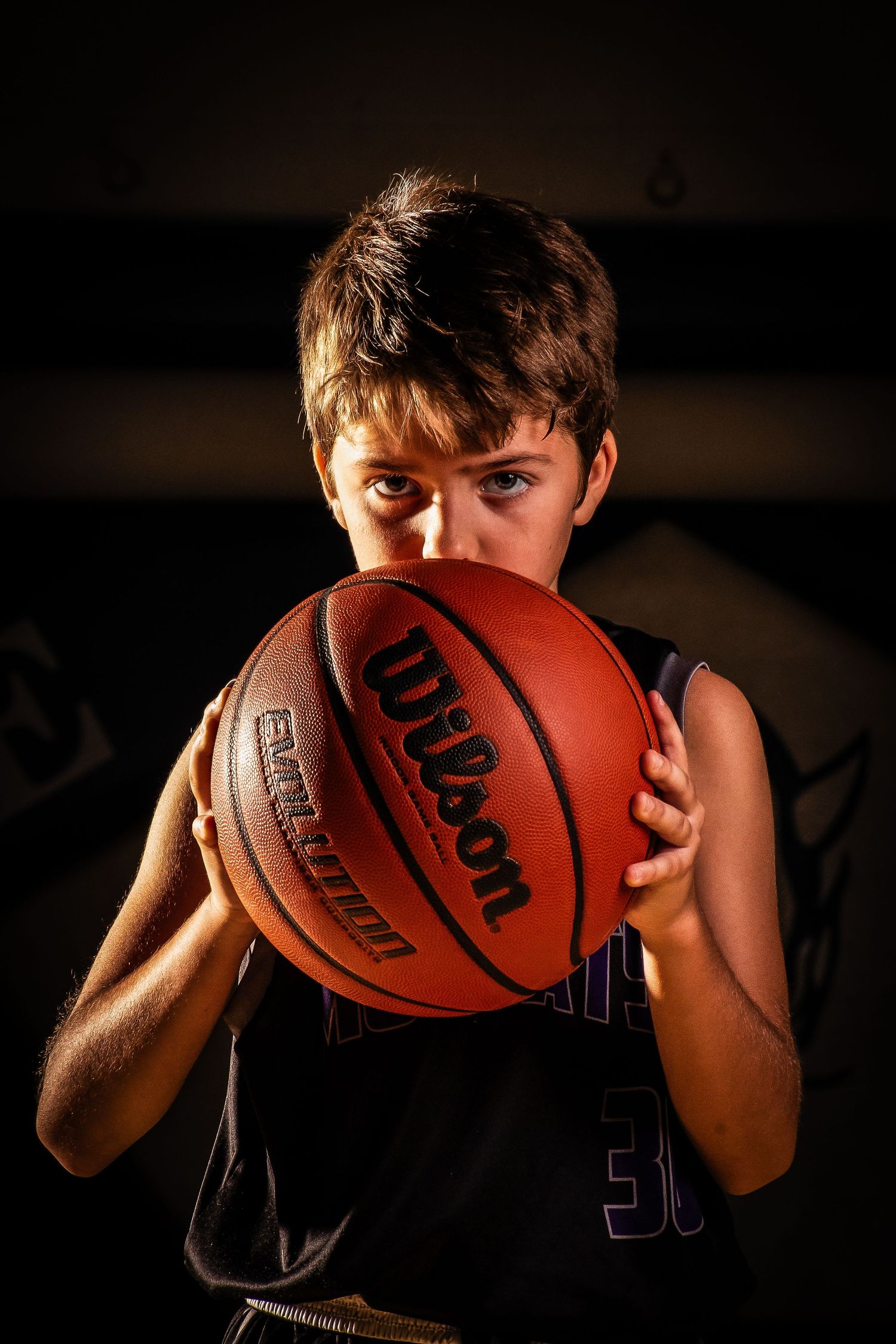 Dramatic close-up photo series of a basketball player holding a Wilson basketball against a dark background.
