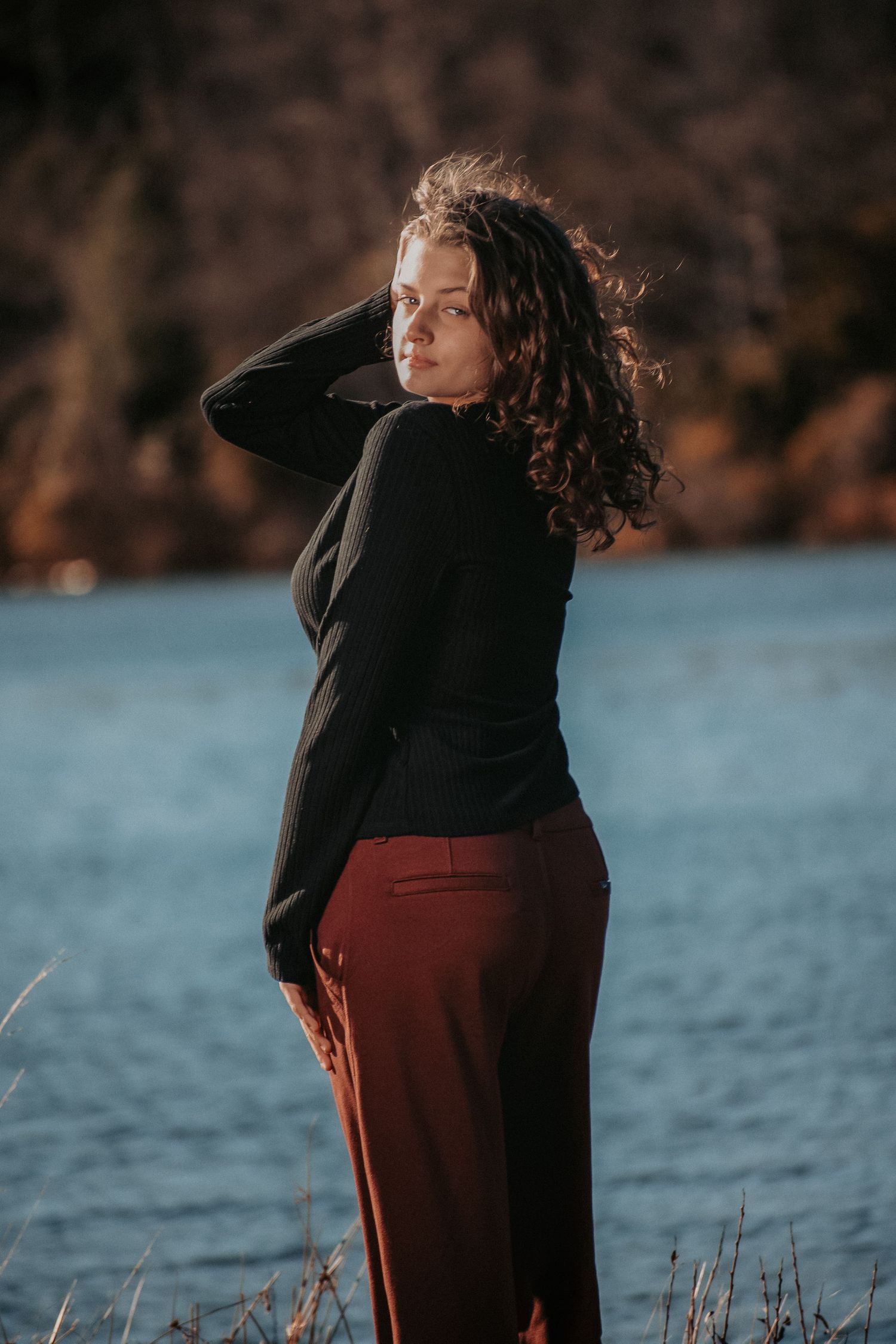 Silhouette of person in black coat against waterfront during sunset.