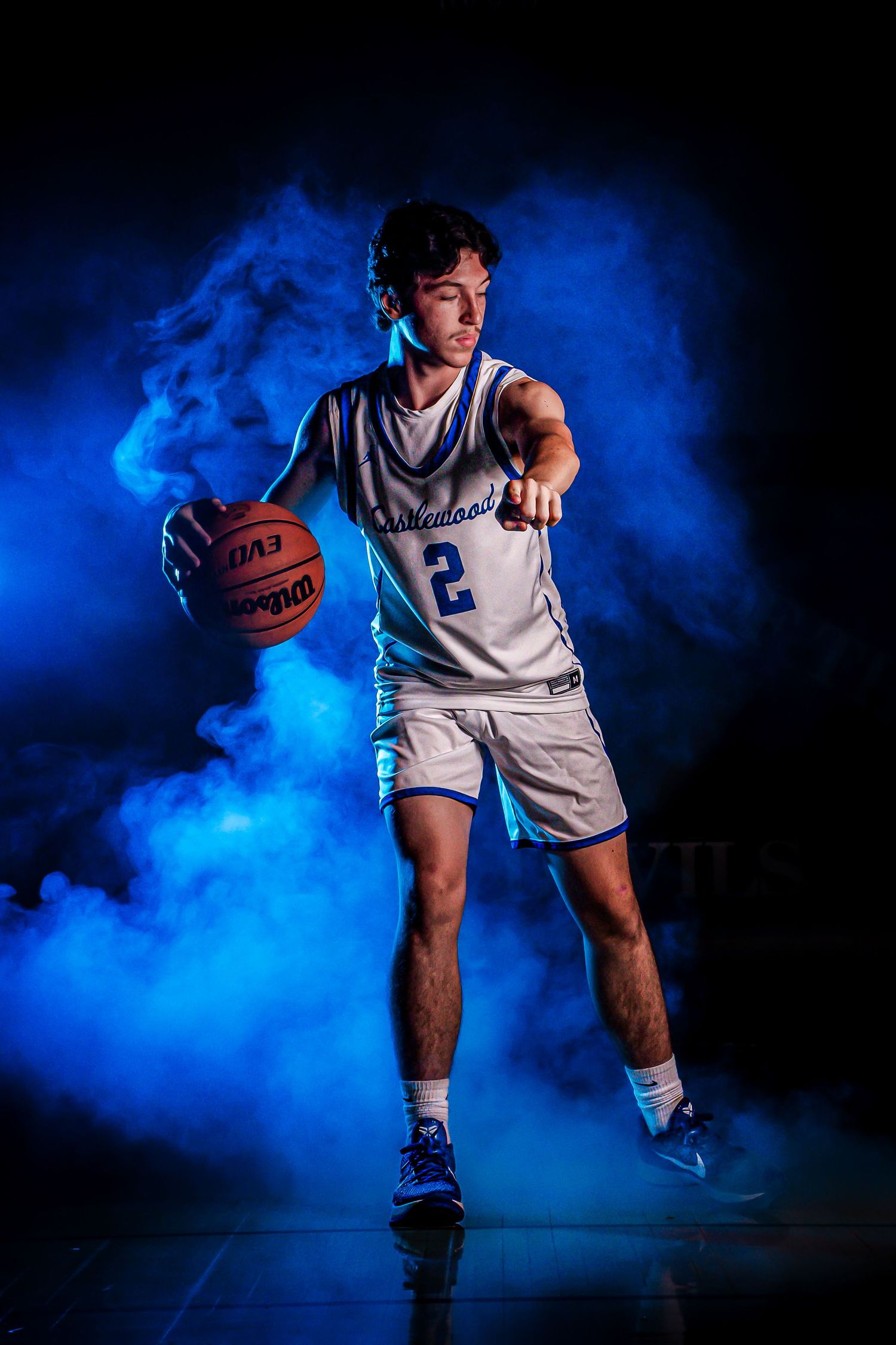 Basketball player demonstrates dribbling skills amid vibrant blue smoke effects on court.
