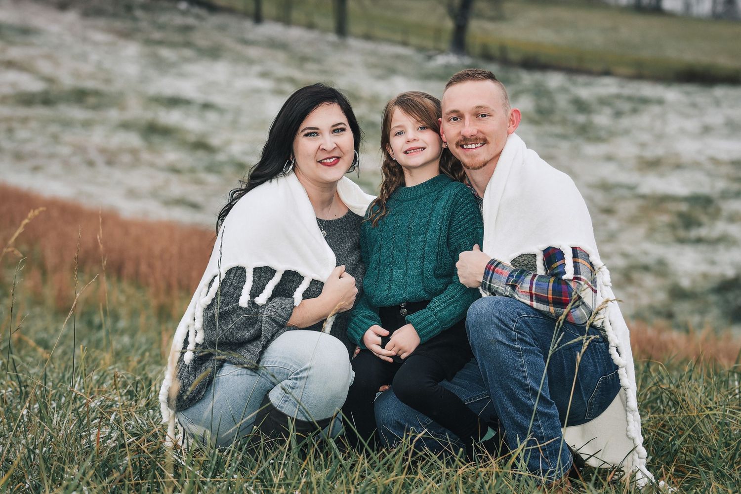 A family sits together on a blanket in a grassy field during an outdoor photo session.