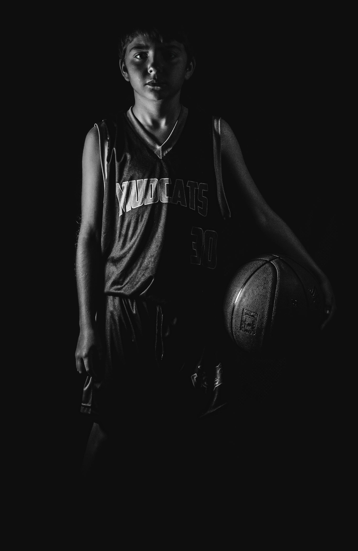 Dramatic black and white portrait of a basketball player in uniform holding a ball against dark background.