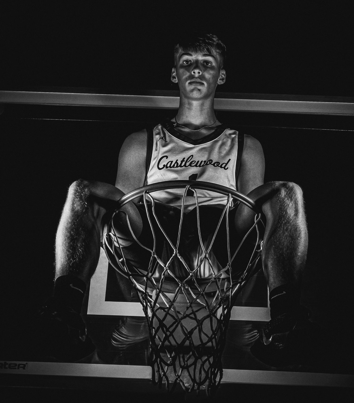 Dramatic black and white portrait of basketball player sitting on basketball hoop.