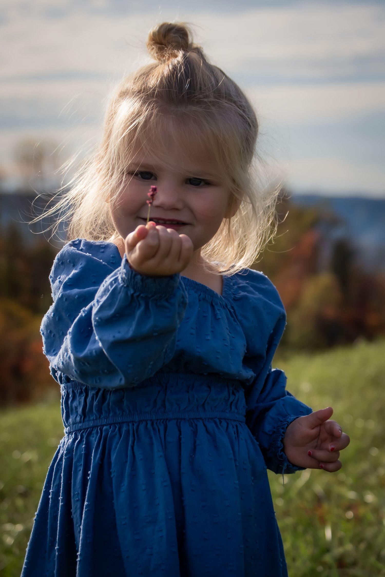 Child wearing blue dress smiles while playing outdoors on sunny day.