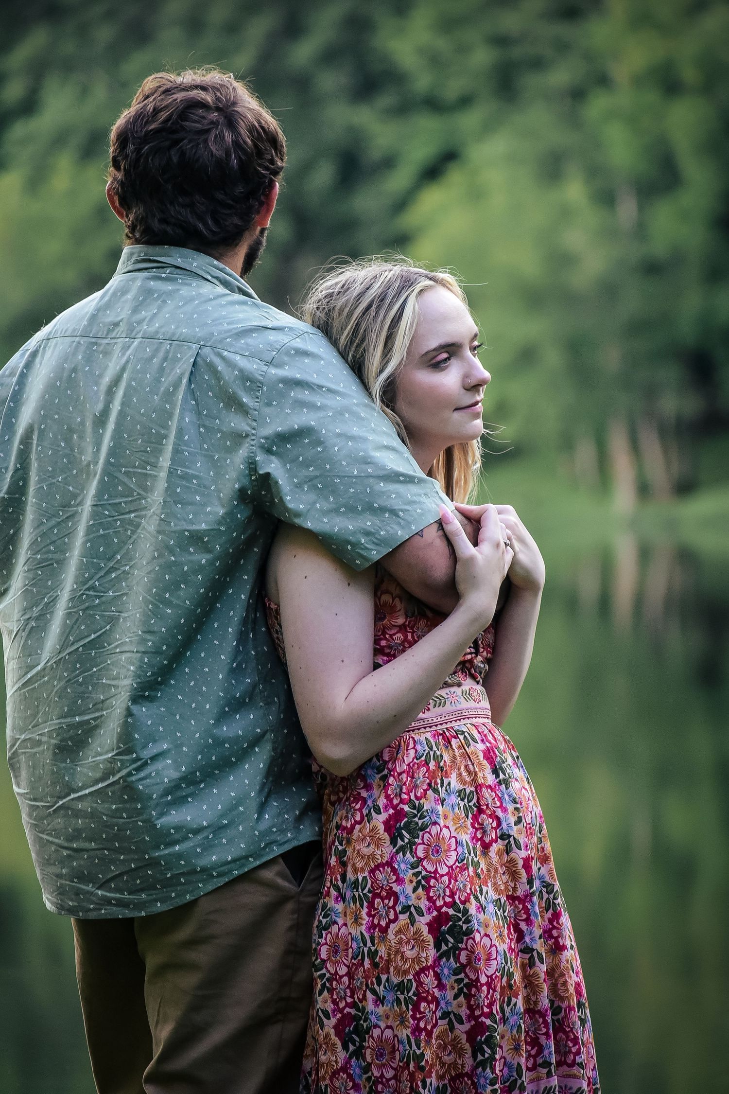 Romantic couple embracing by a serene lake with soft natural lighting.
