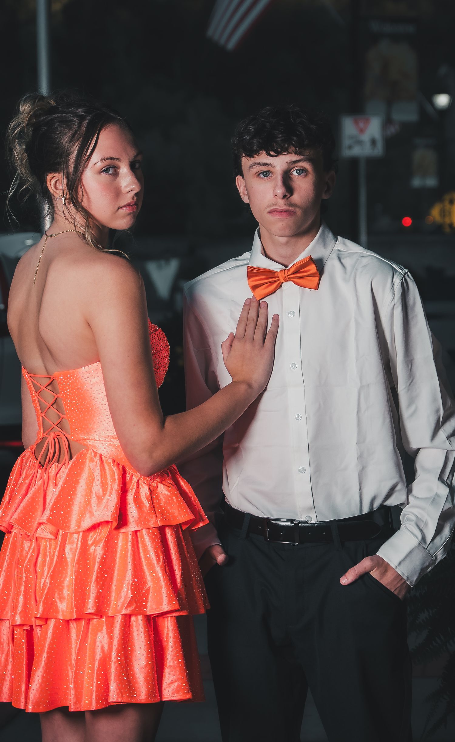 Couple in formal attire dancing at a party, with the woman wearing a bright coral ruffled dress and man in white shirt.