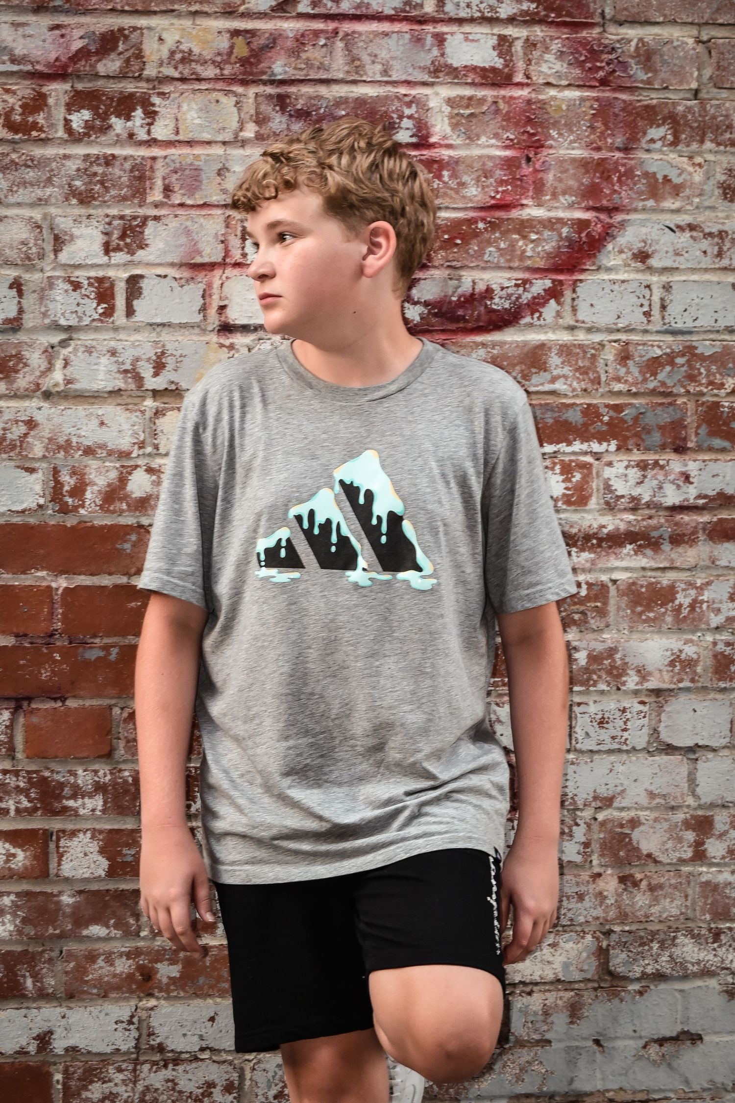 A person wearing a gray t-shirt with mountain design stands against a weathered brick wall background.