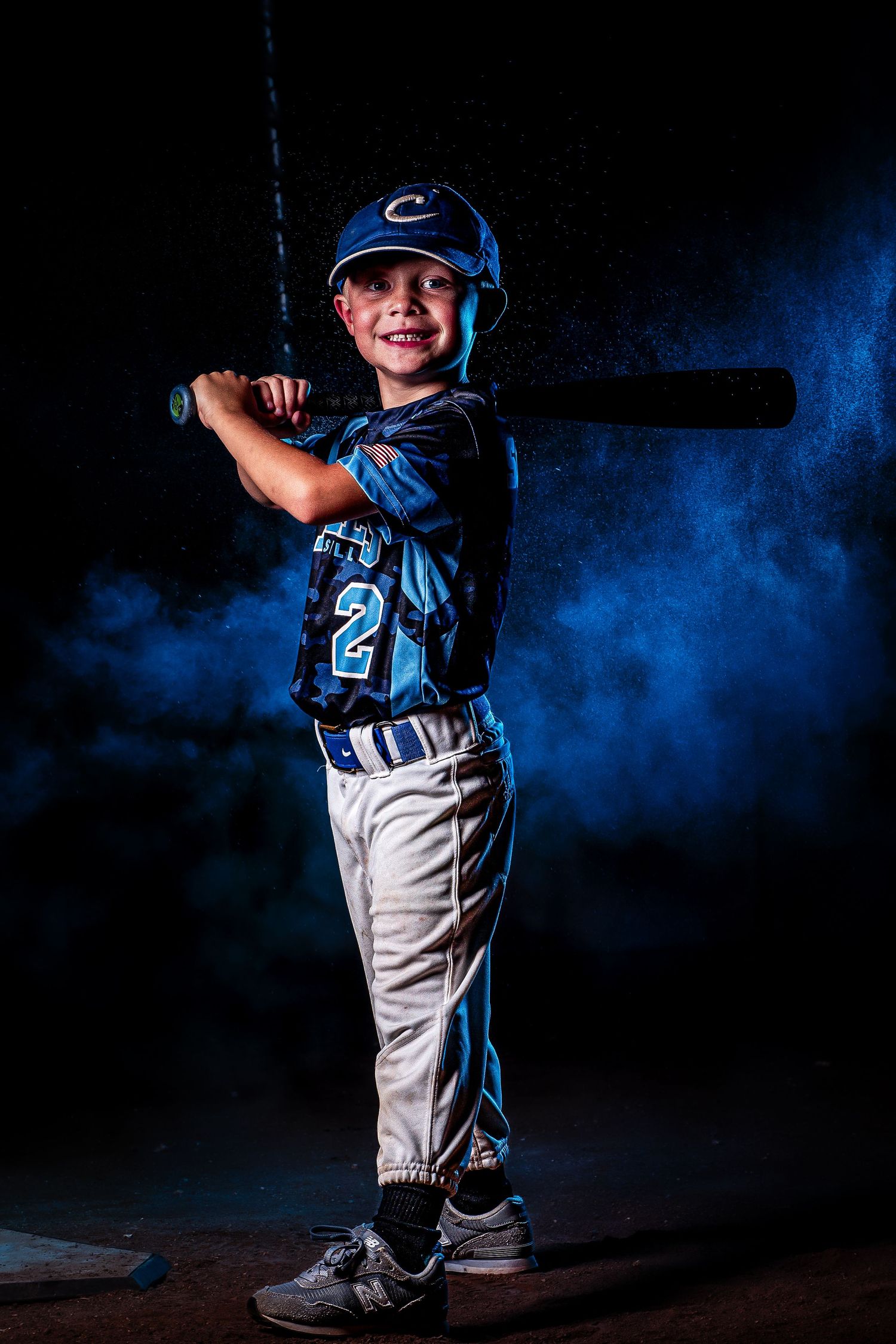 Youth baseball player poses in uniform against blue smoke background effect.