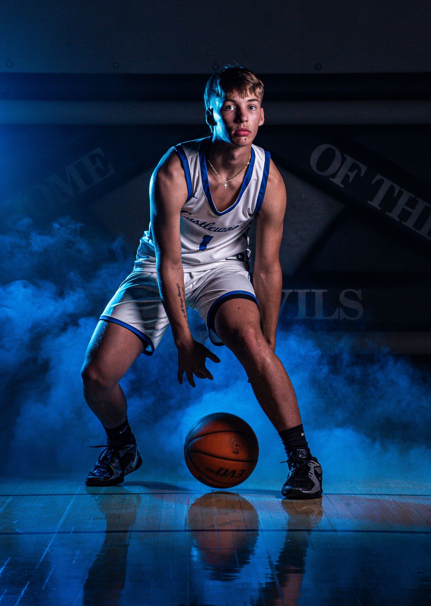 Player in white jersey performs dribbling drill on basketball court with blue smoke effects.