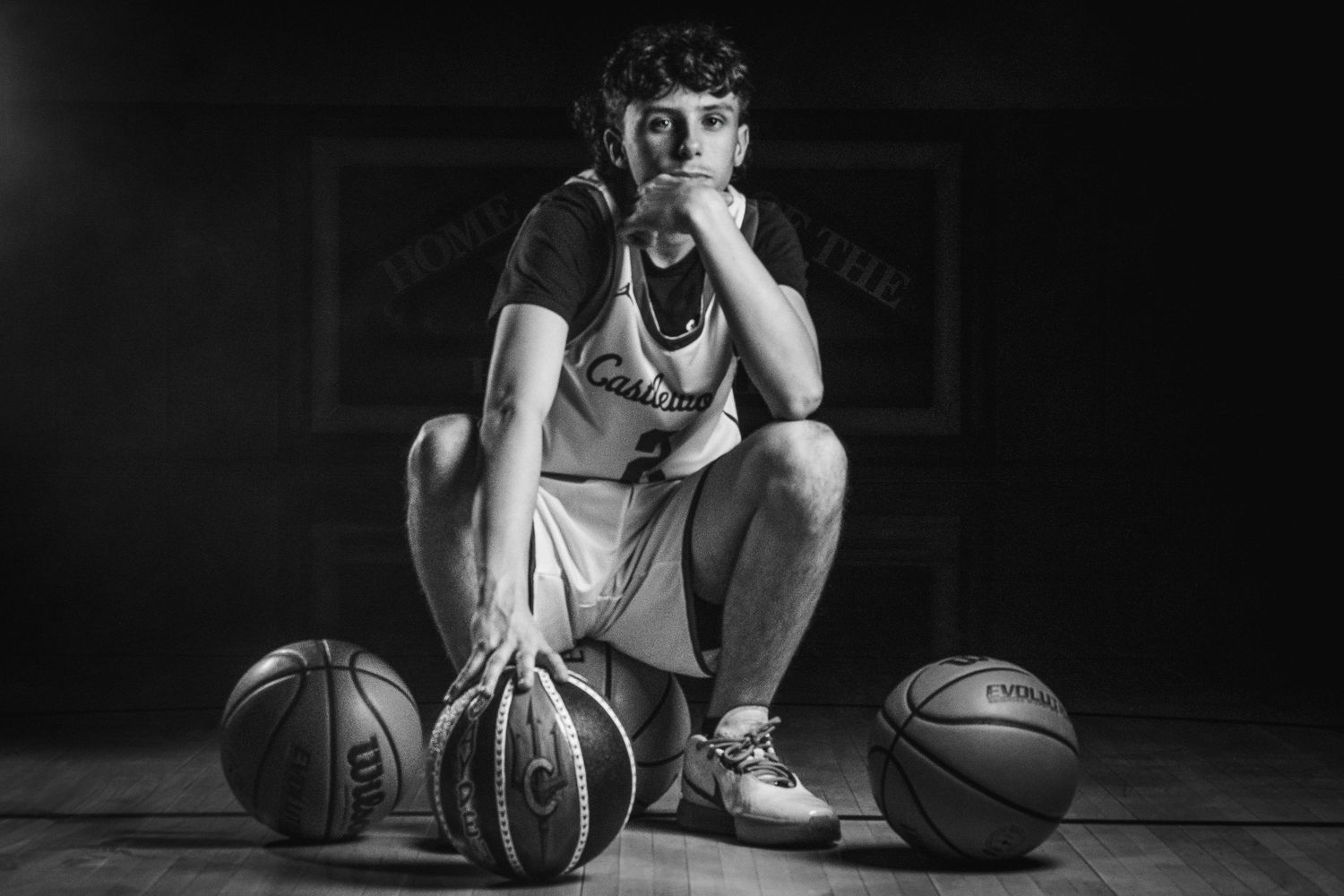 Side view of basketball player sitting on wooden floor in black and white.