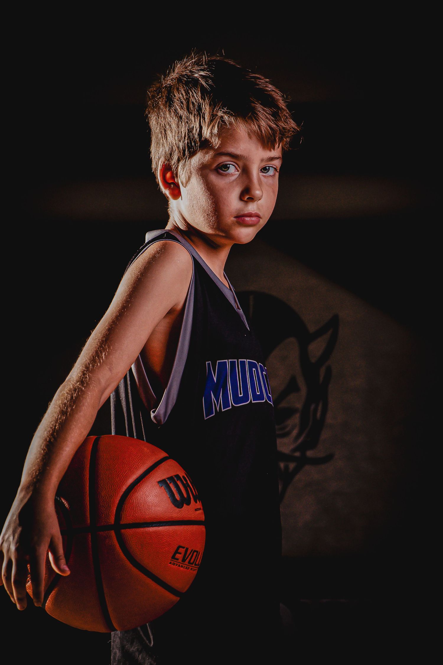 Young basketball player in purple Wildcats jersey posing with basketball in dramatic lighting.