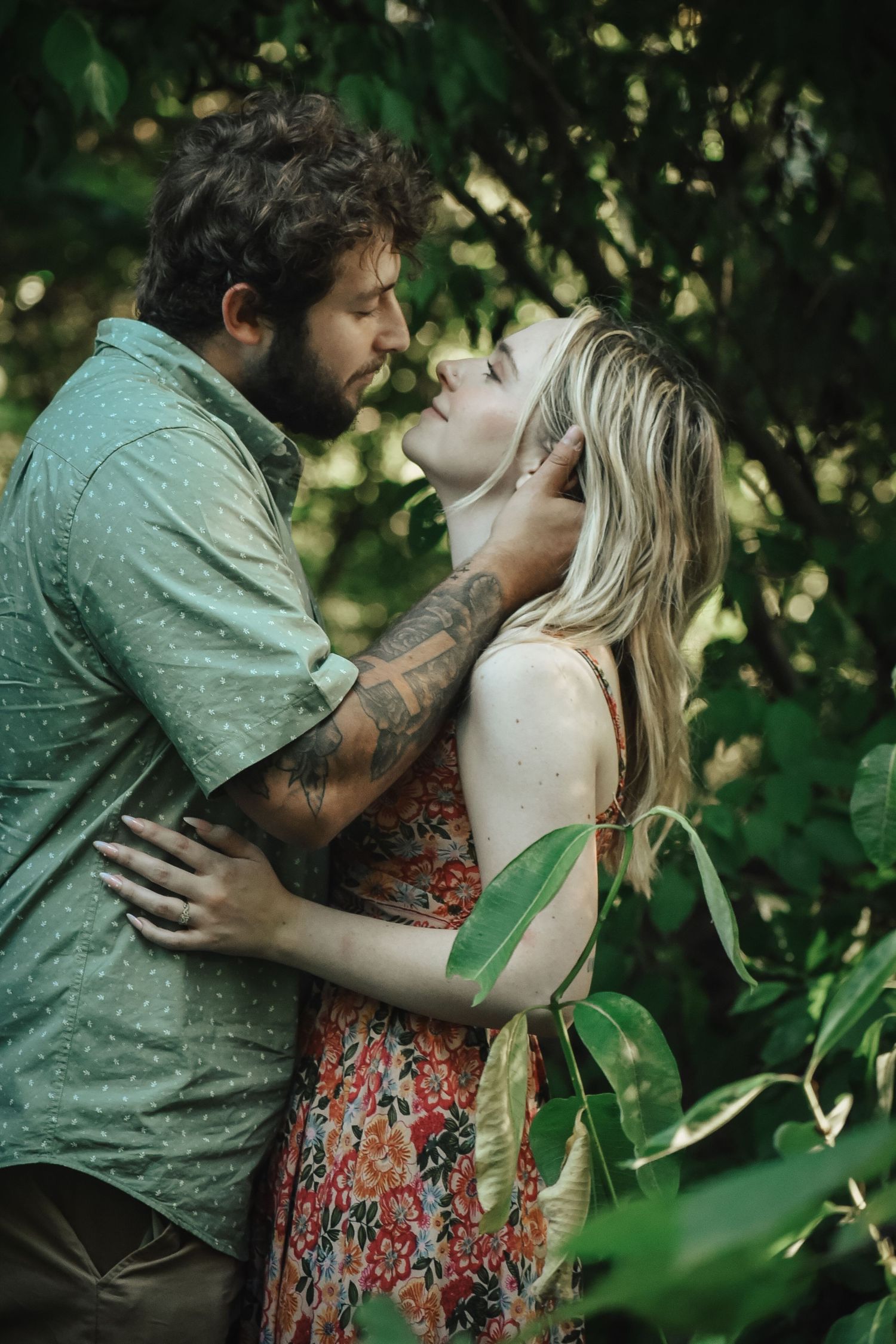 A couple embraces in a lush green setting with sunlight filtering through the leaves.