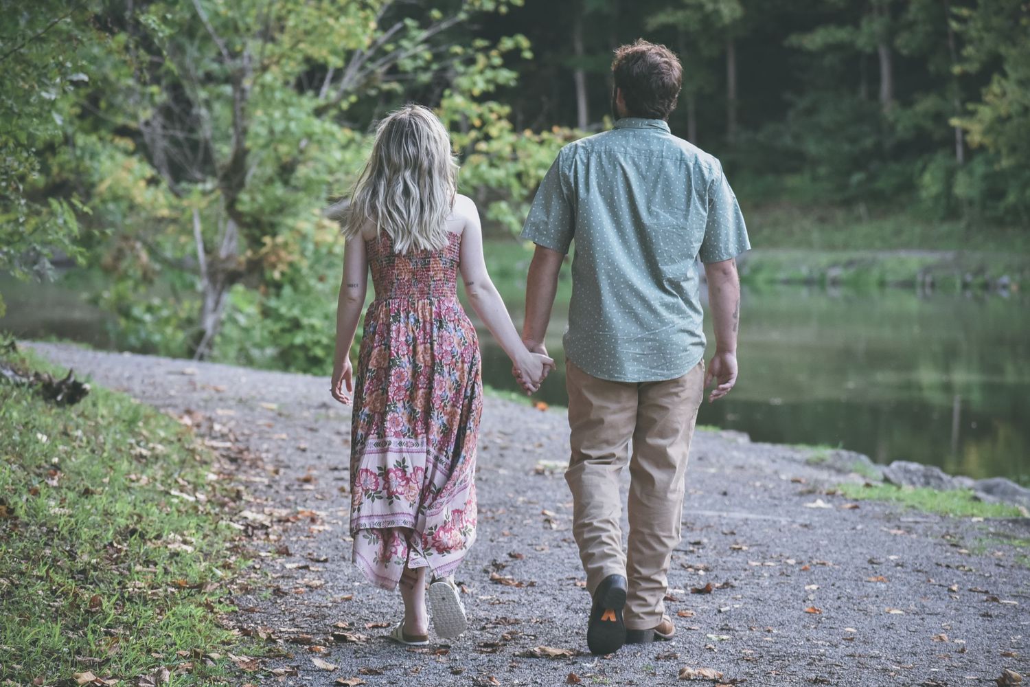 Two people walking hand in hand on a scenic trail next to a peaceful lake.