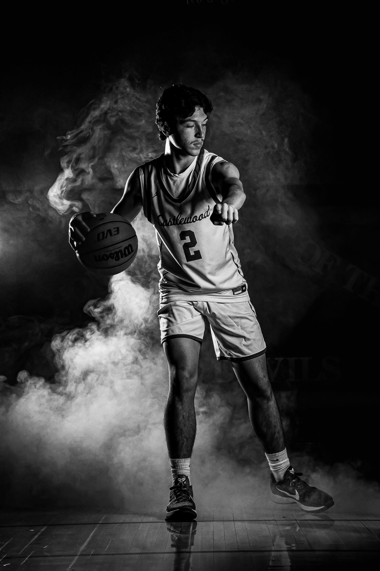 Basketball player moves through dramatic smoke effects in black and white photography.