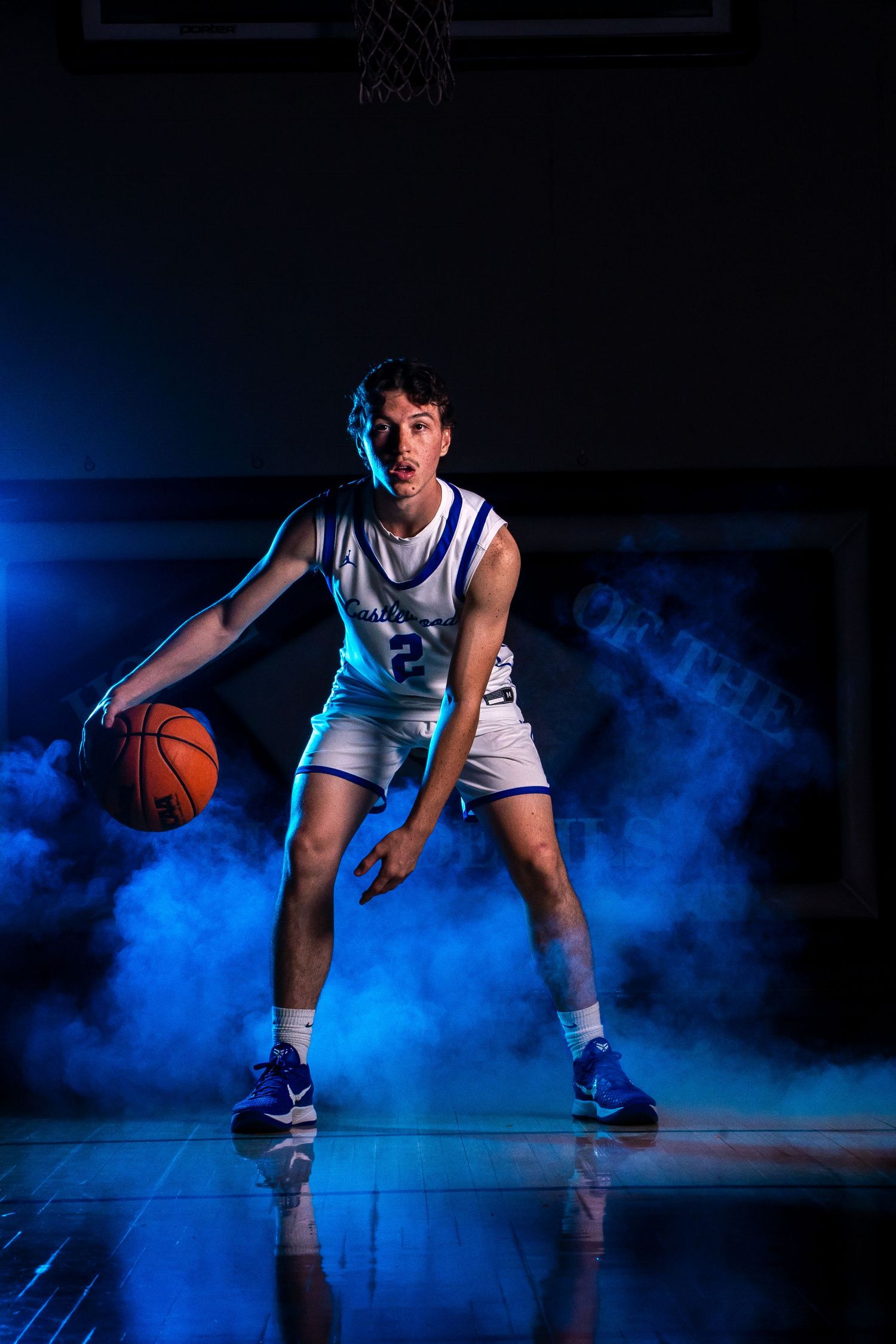 Basketball player in white uniform dribbling on court surrounded by dramatic blue smoke effects.