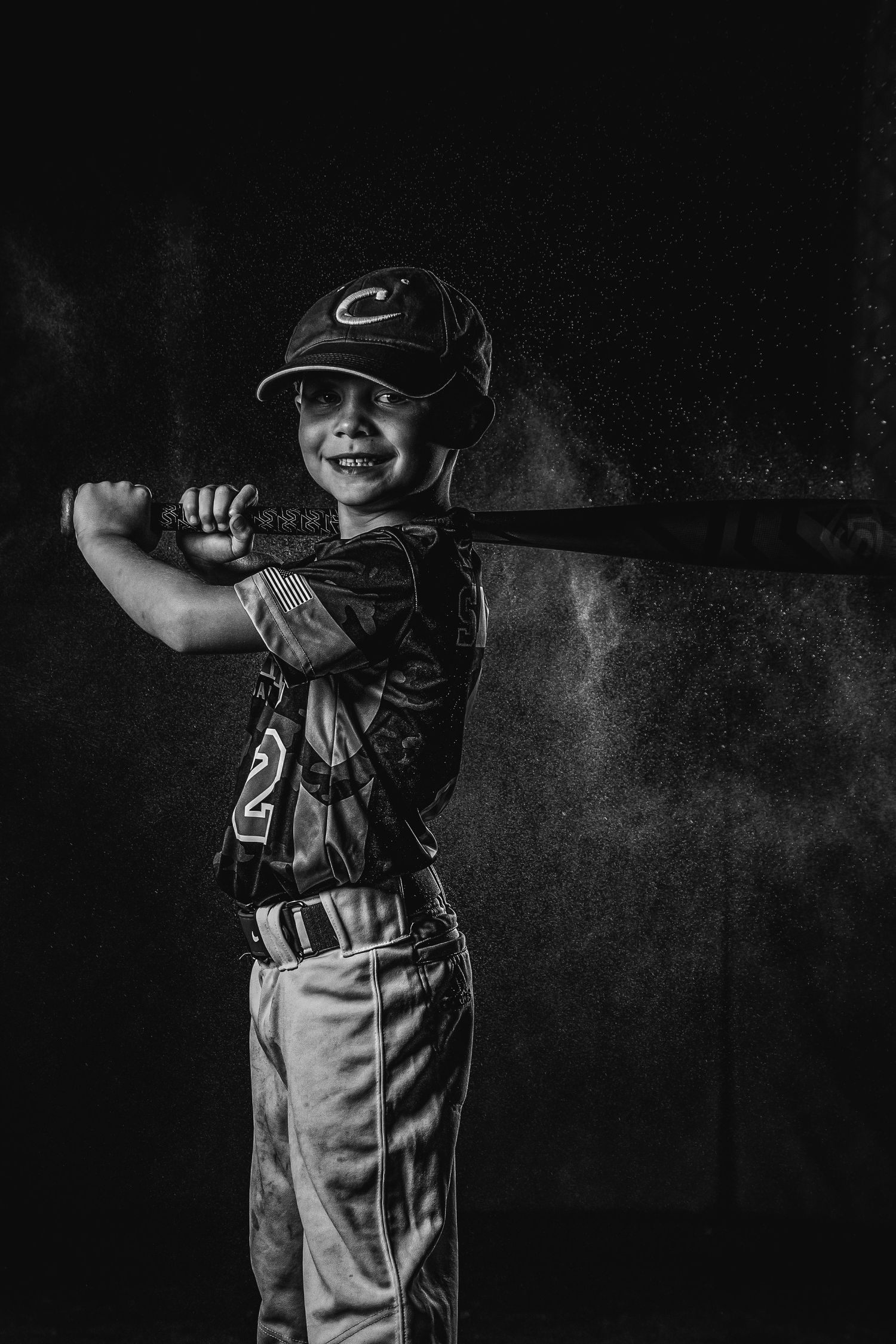 Baseball player in uniform holds bat in dramatic black and white lighting.