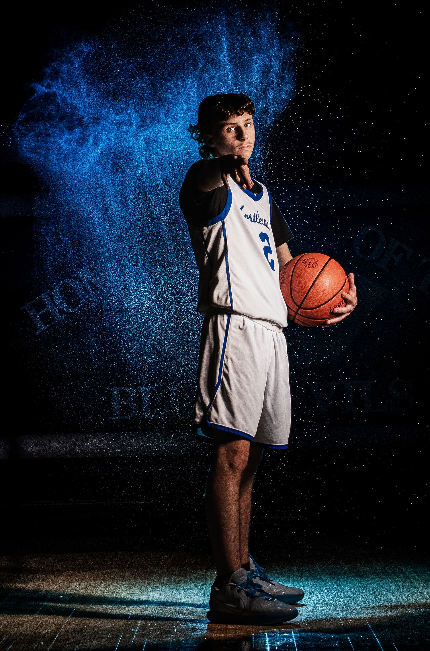 Basketball player poses with ball against blue-lit backdrop in dramatic lighting.