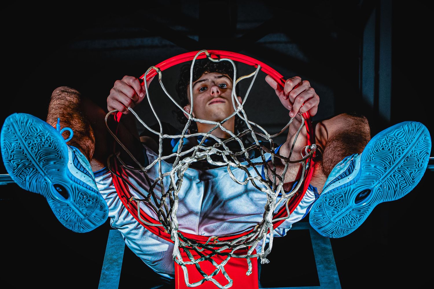 Low angle view of basketball hoop with blue lighting effects and dramatic shadows.