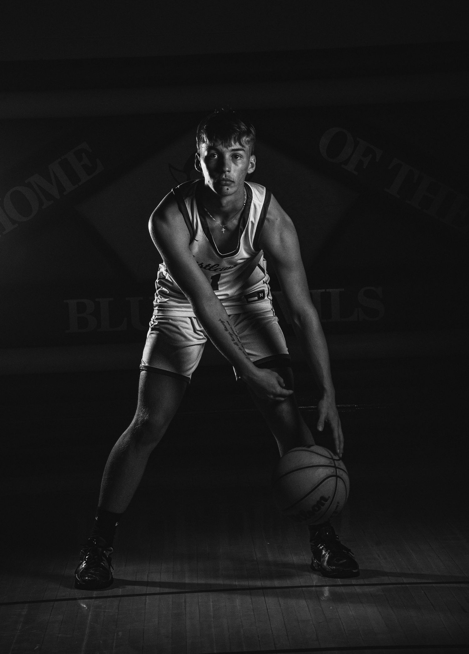 Low angle shot of basketball player dribbling on hardwood court in dark setting.