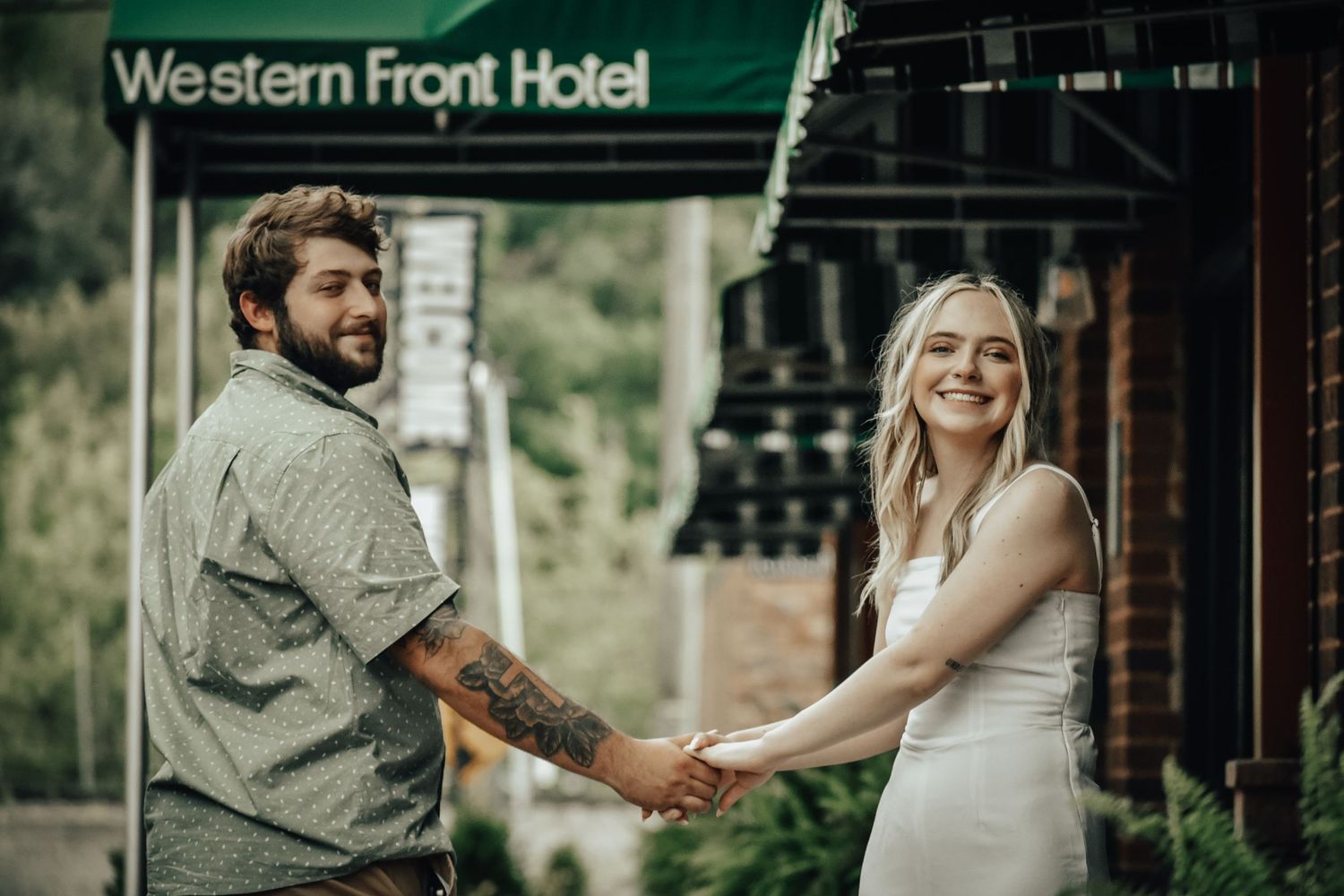 A couple poses in front of the Western Front Hotel sign during an engagement session.