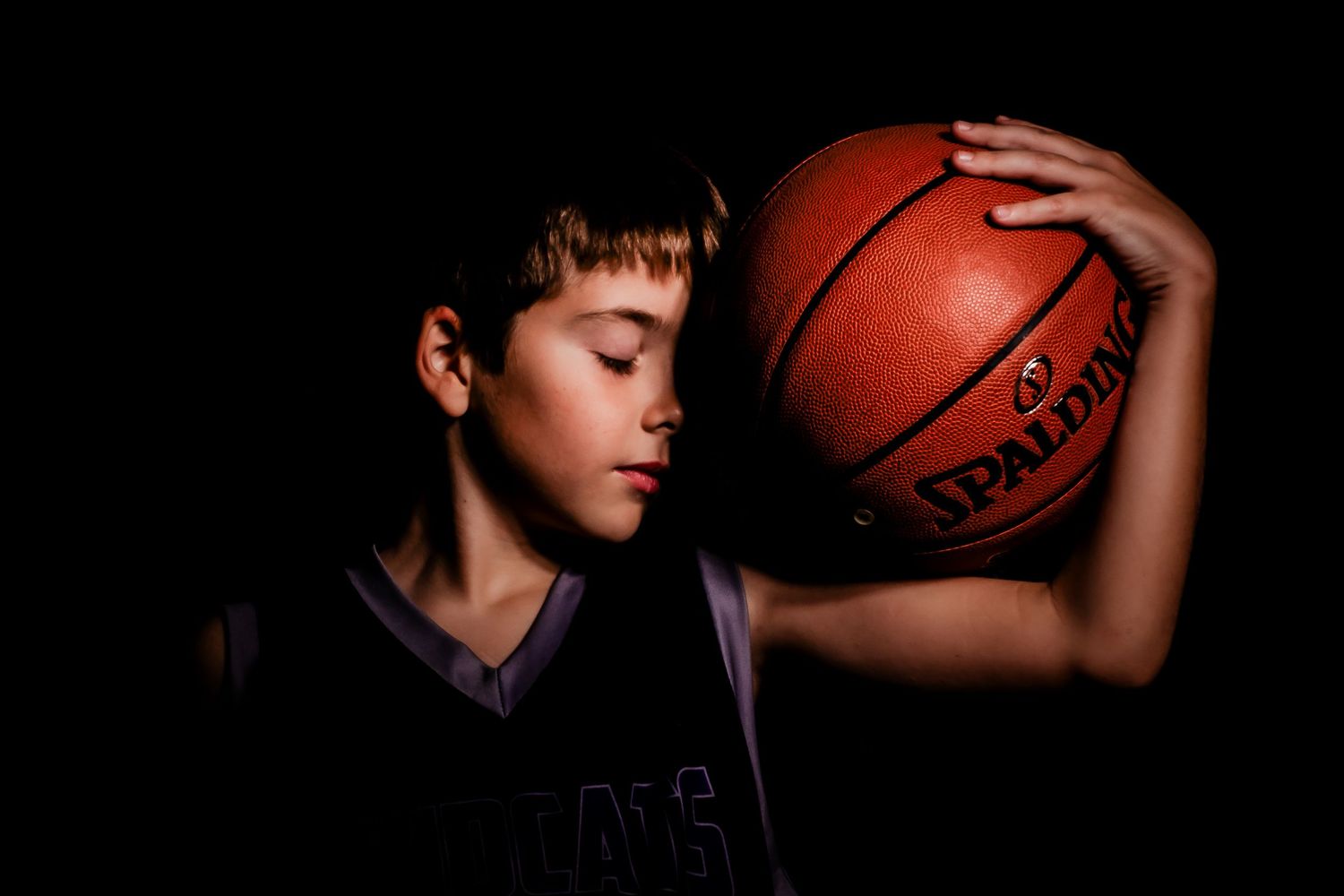 Basketball player silhouetted against dark background holding ball in dramatic lighting effect.