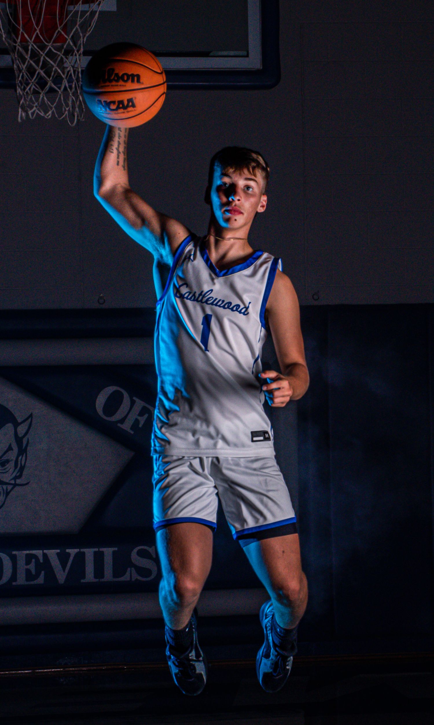 Player leaps with basketball in dramatic action shot with blue lighting effects.