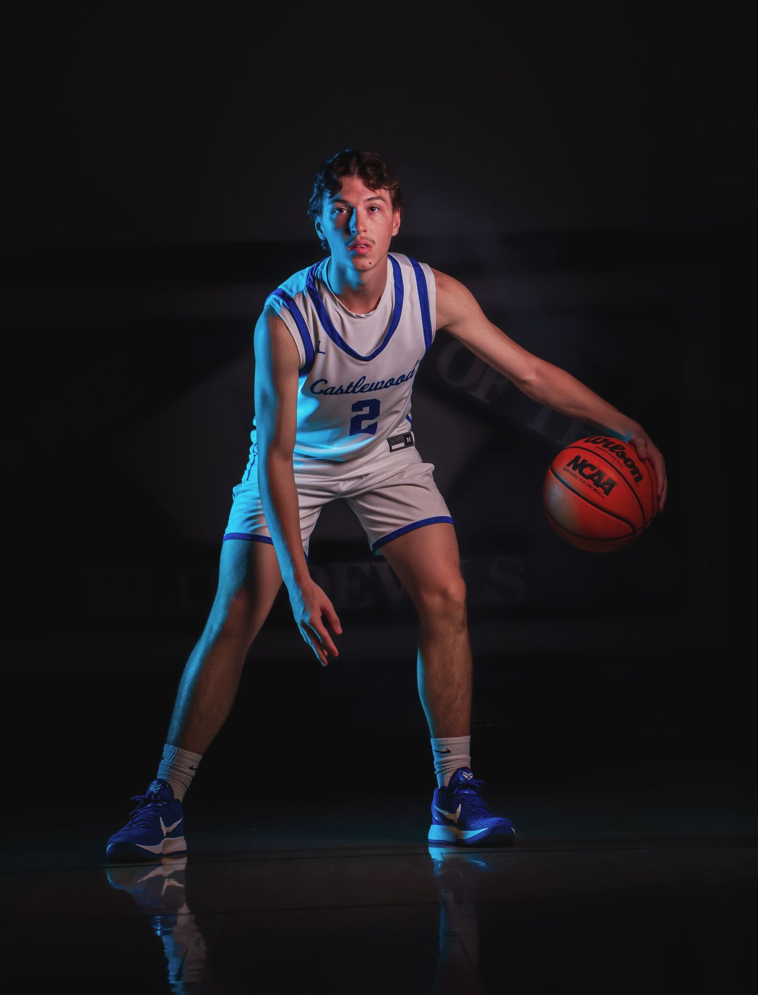 Basketball player in defensive stance illuminated by dramatic blue lighting.