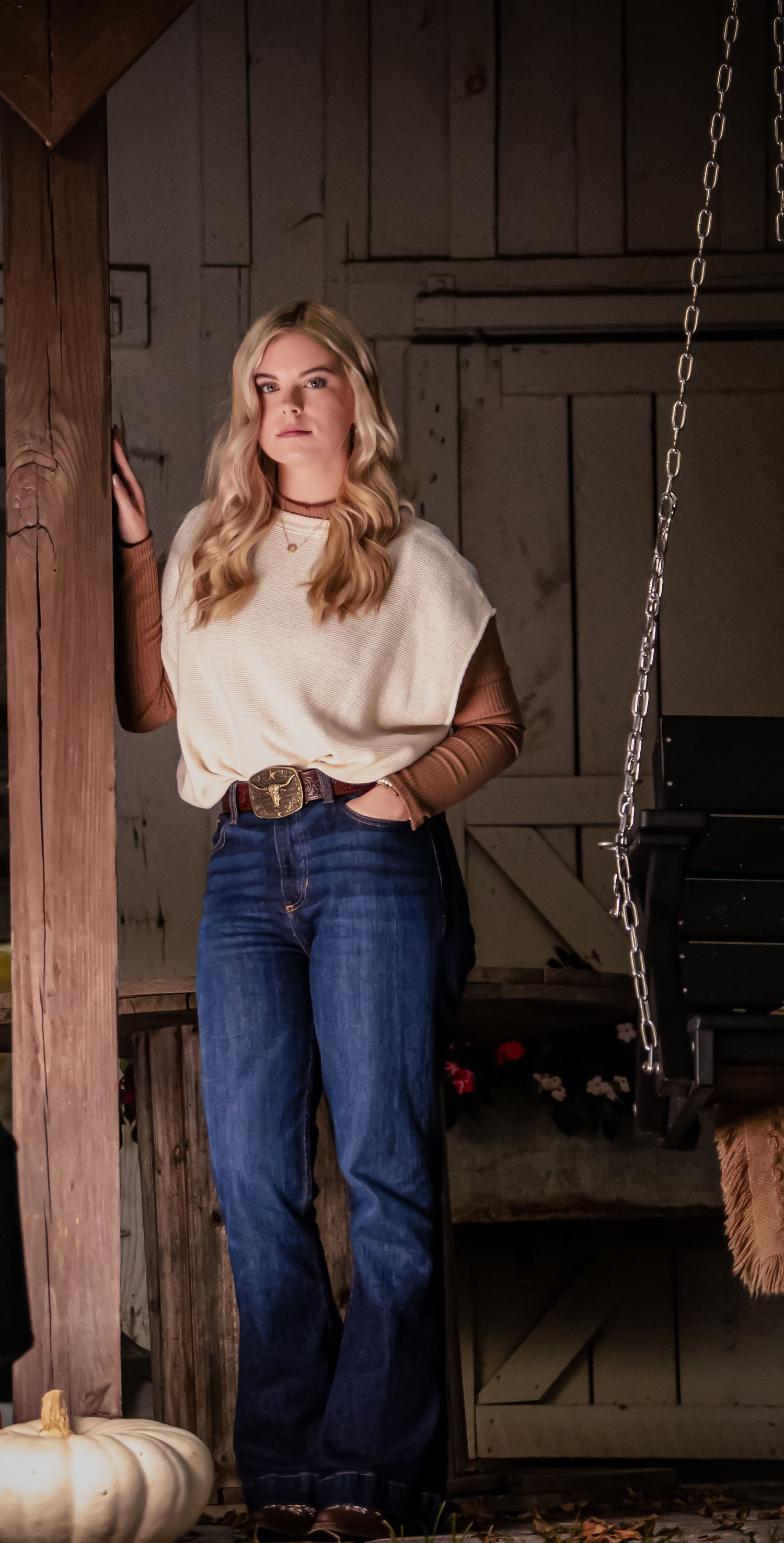 Autumn fashion photo with cream sweater, jeans and decorative pumpkin in rustic barn setting.