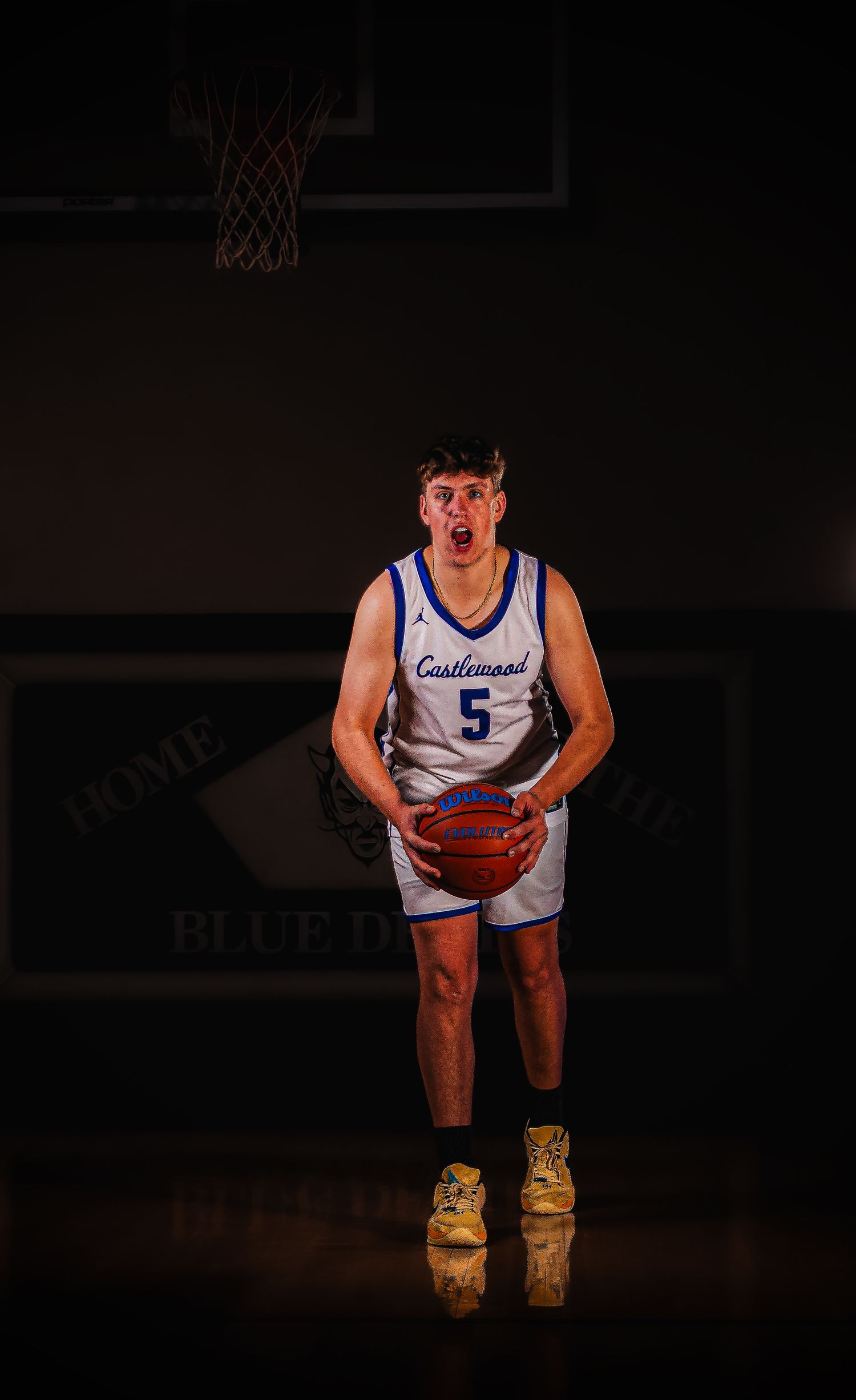 Basketball player in white Castlewood uniform crouches in dramatic lighting against dark background.