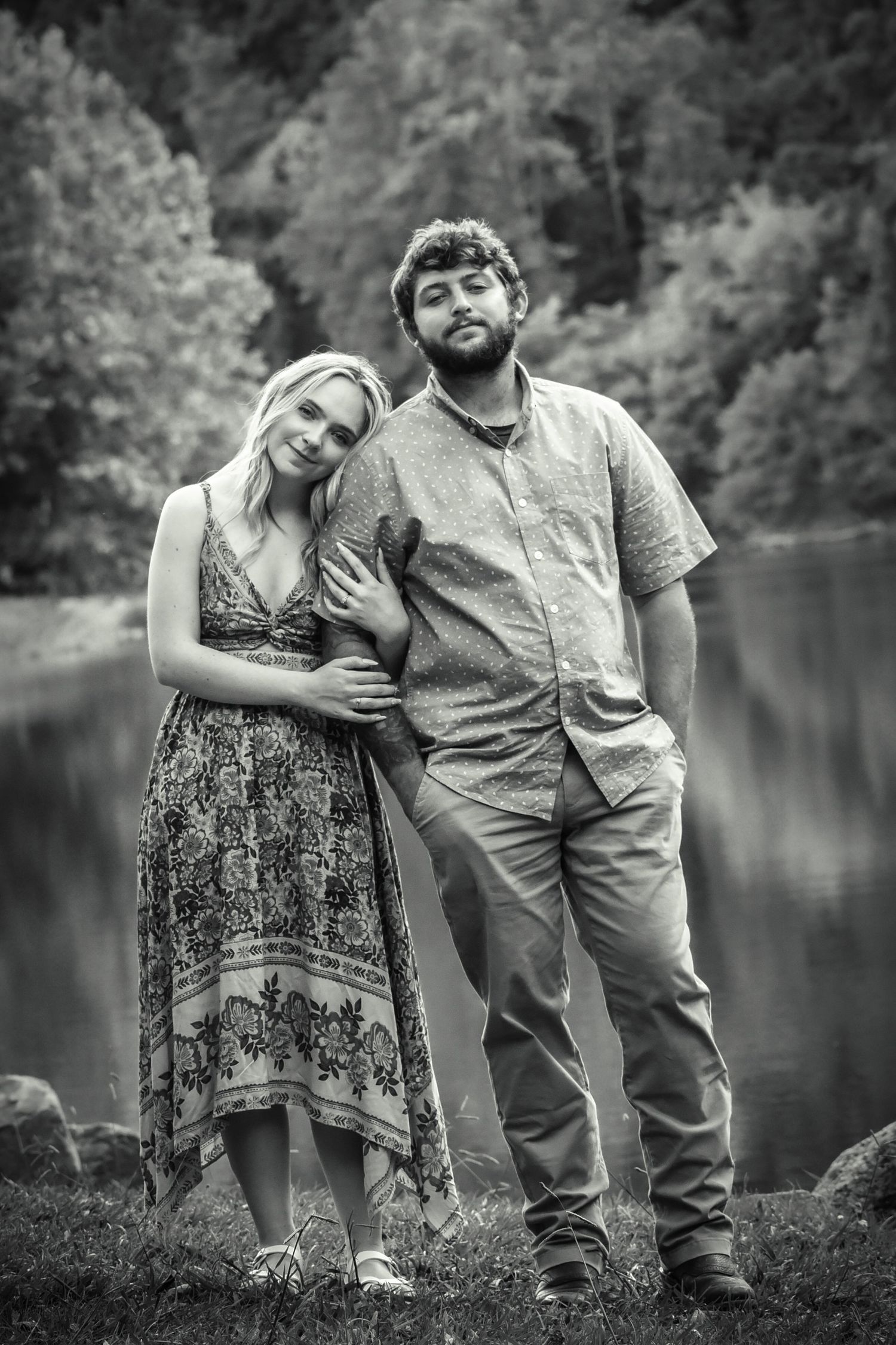 A black and white portrait of a couple posing playfully by a lake.