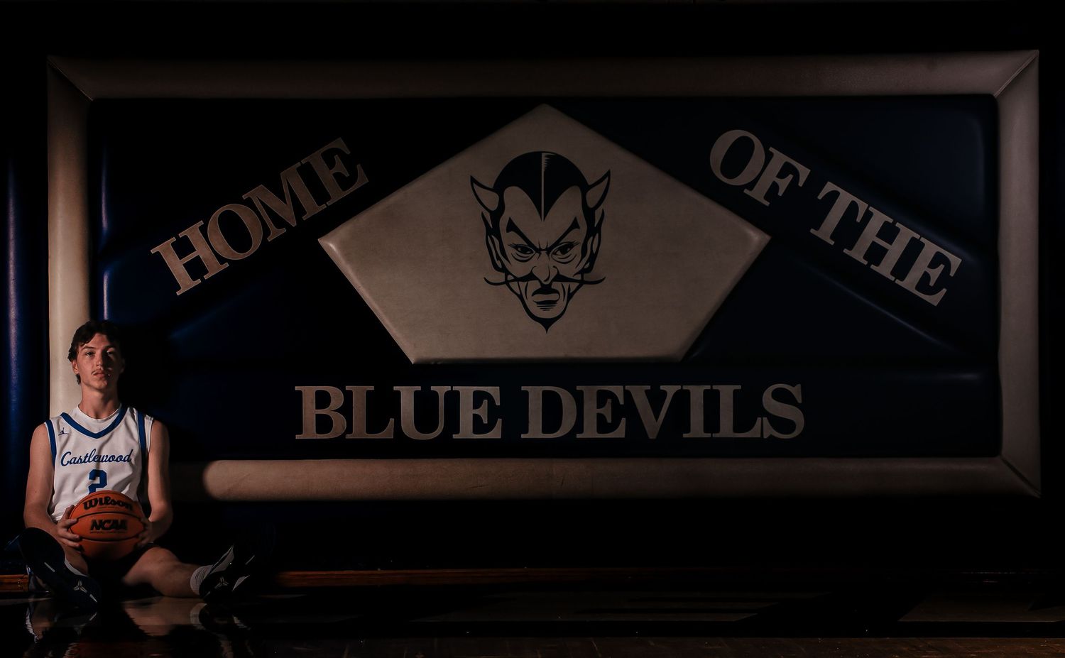Player poses with basketball under illuminated Blue Devils team sign.
