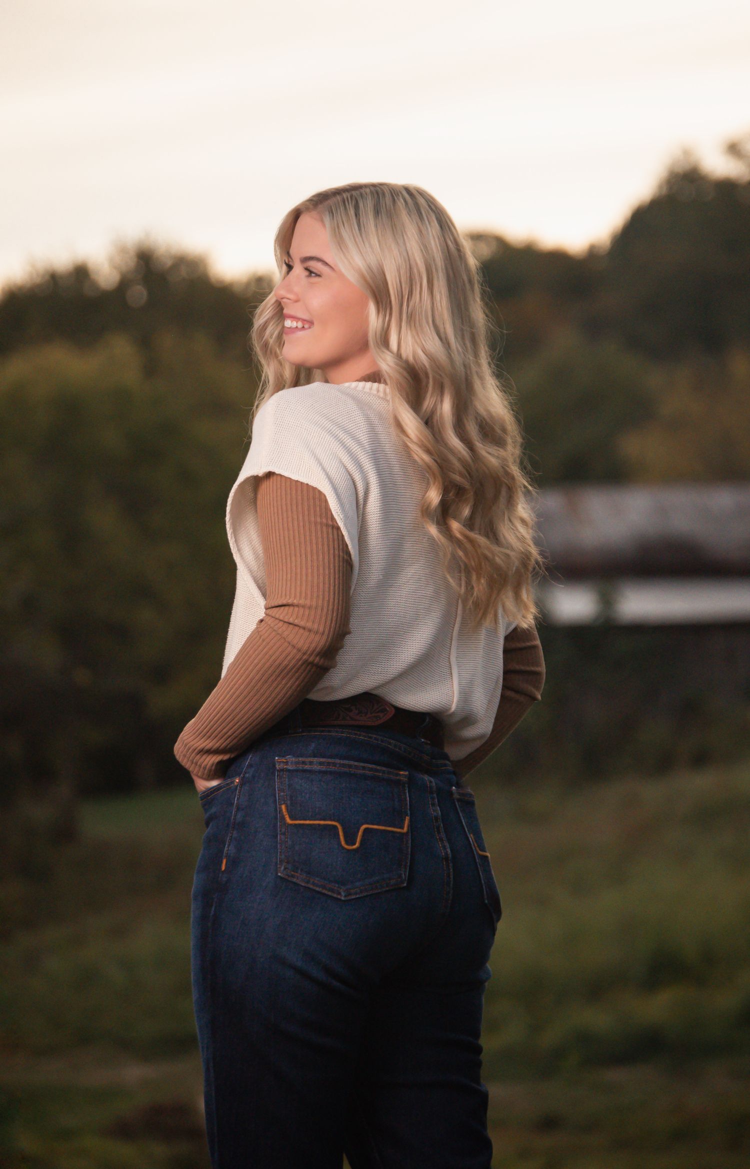 Woman wearing white top and dark jeans photographed from behind during sunset.