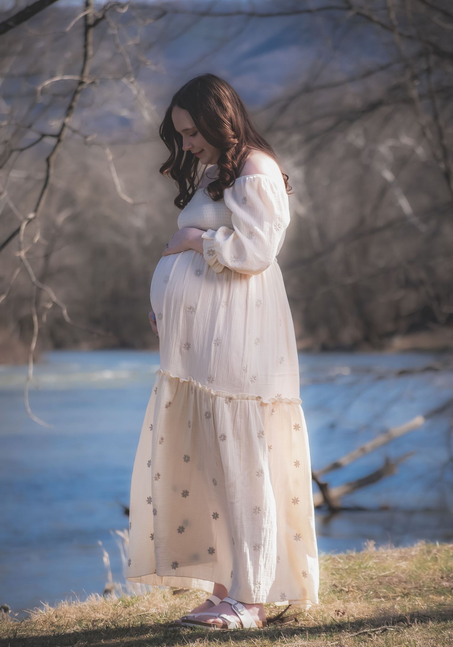 A figure in a flowing white dress stands near a lake on a winter day, creating a serene and ethereal scene.