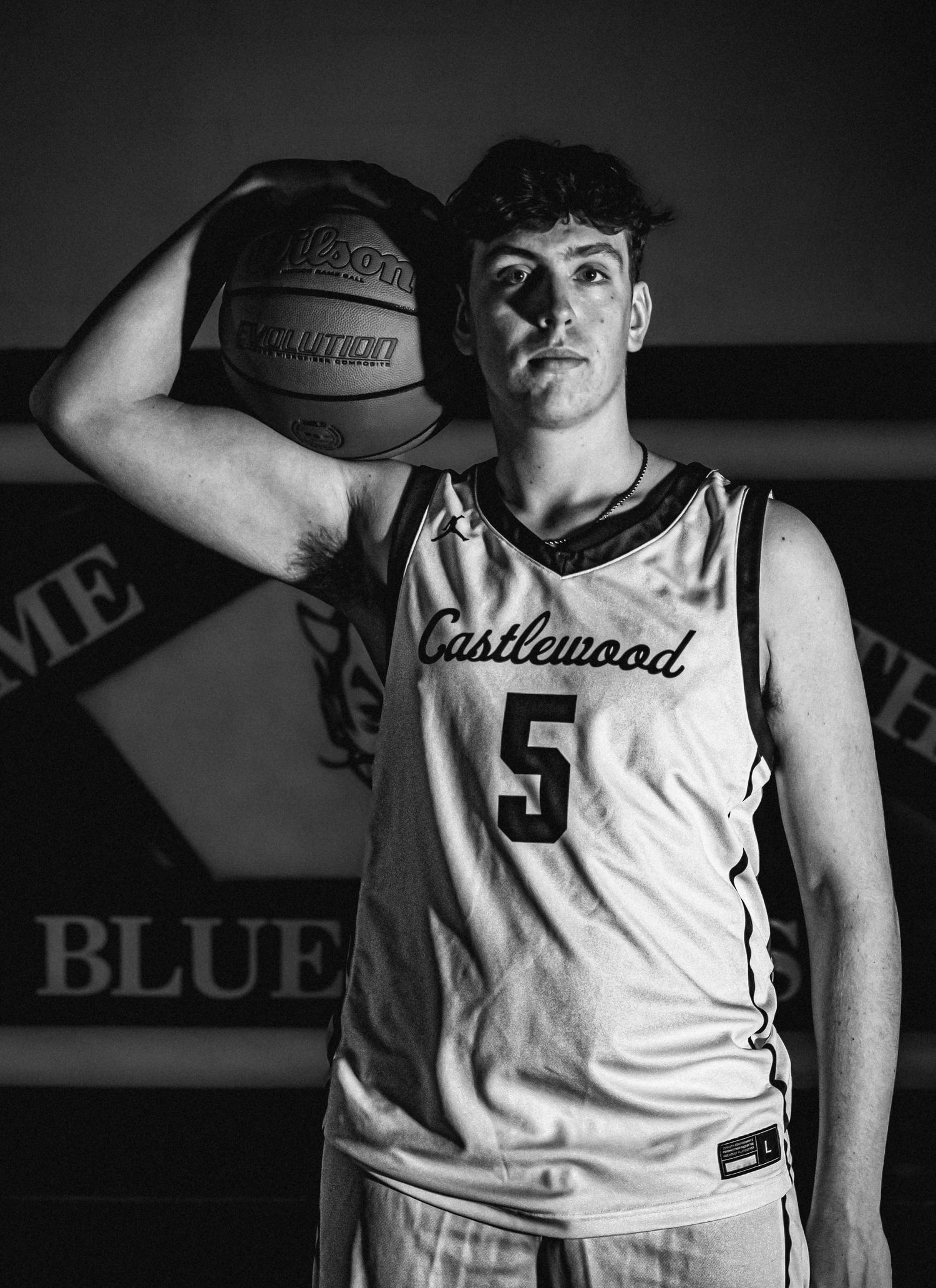 Black and white portrait of a basketball player in a Castlewood #5 jersey holding a basketball against a dark background.