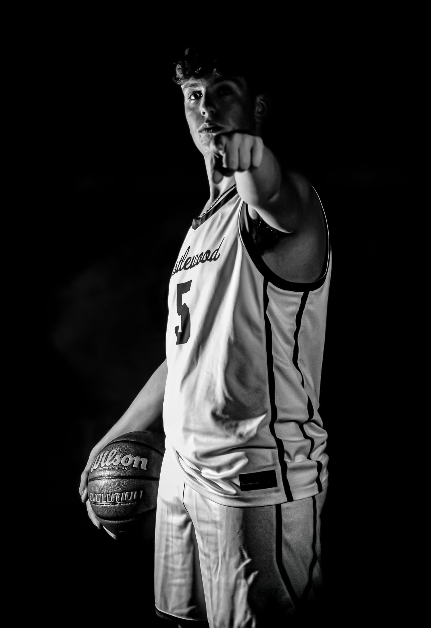 Black and white photo of a basketball player in jersey number 5 holding a ball and pointing forward.