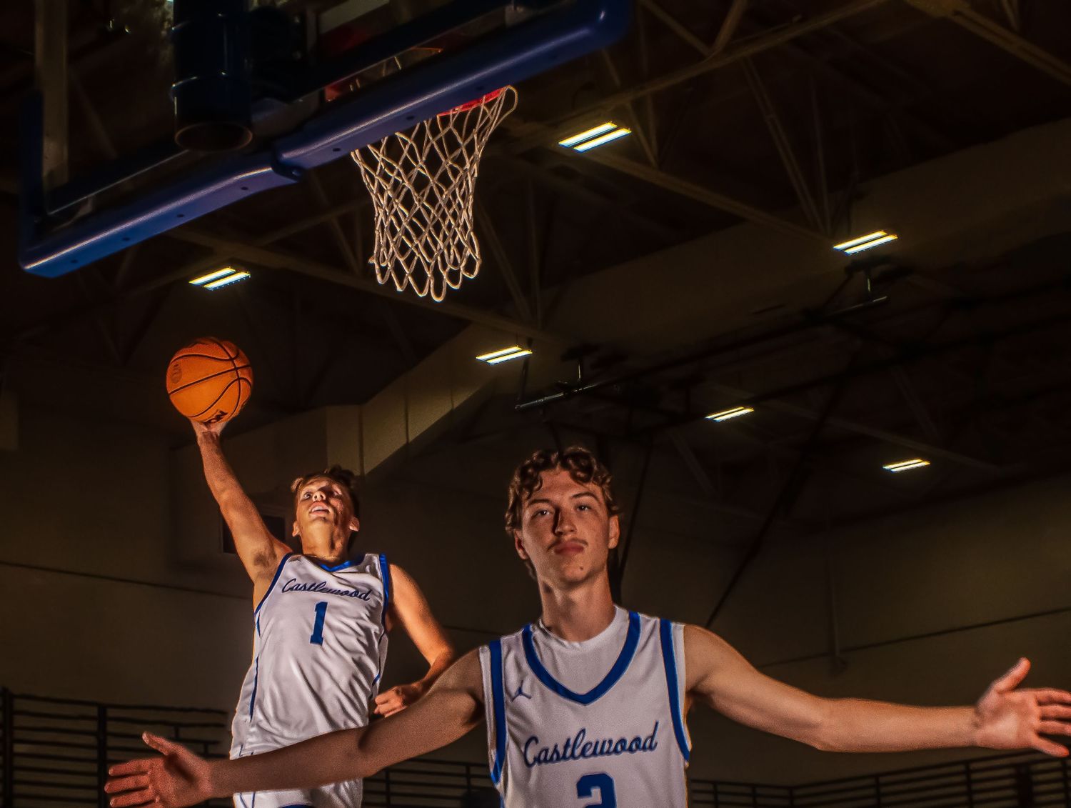 Basketball players practice offensive moves in gymnasium setting.