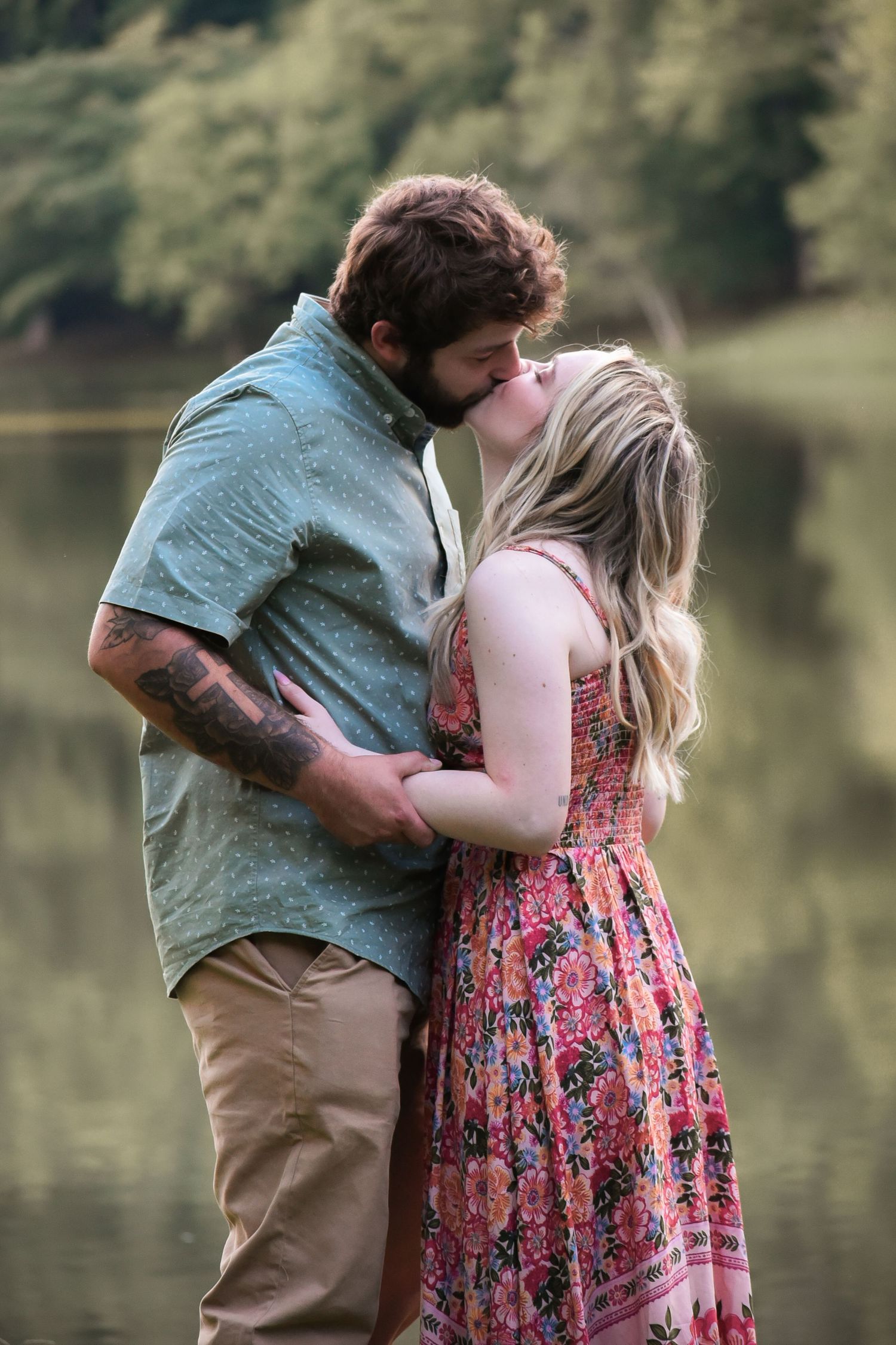 An intimate moment captured between a couple by a tranquil lake in natural setting.