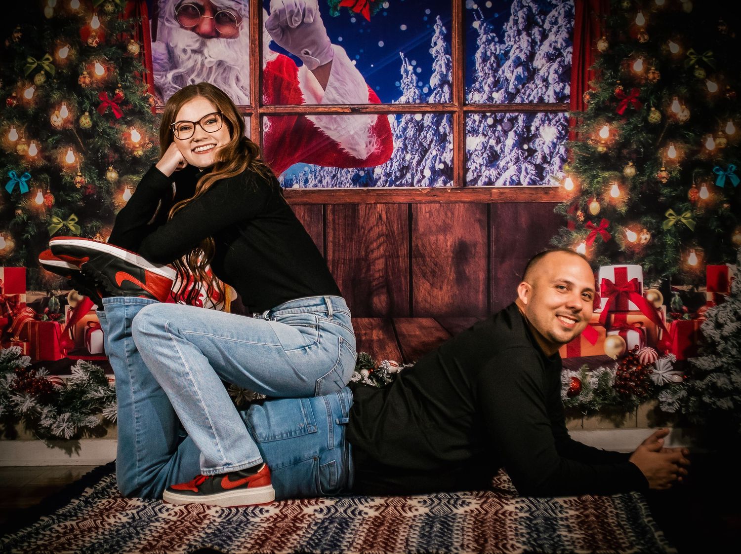 A festive holiday photoshoot setup with rustic wooden backdrop, Christmas trees, and twinkling lights.