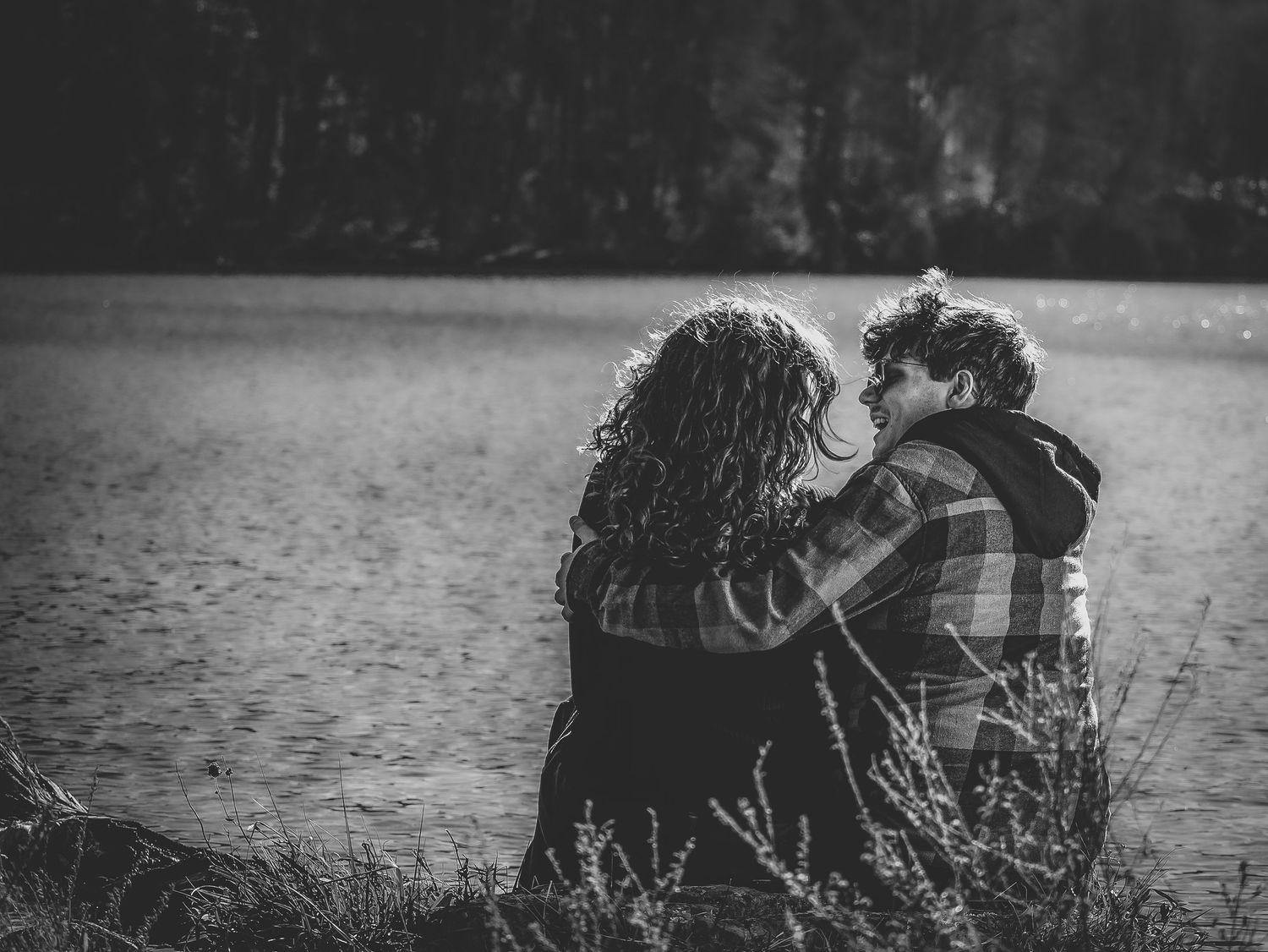 A couple sits together on a dock by a serene lake during sunset creating a romantic silhouette against the water.