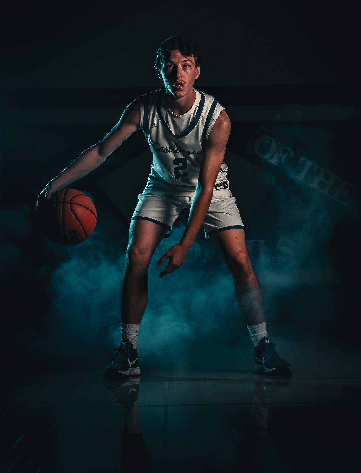 Low angle shot of basketball player in defensive position with atmospheric smoke effects.