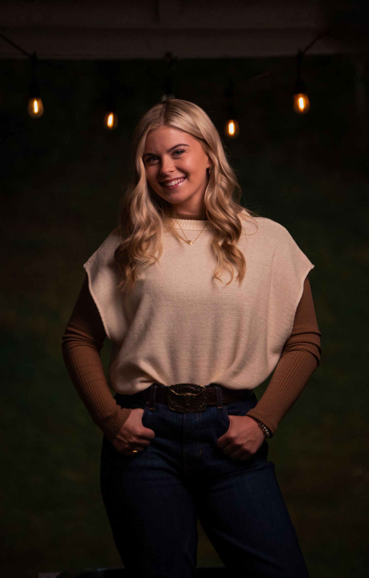 Fashion portrait with hanging lights featuring cream top and dark denim in moody setting.