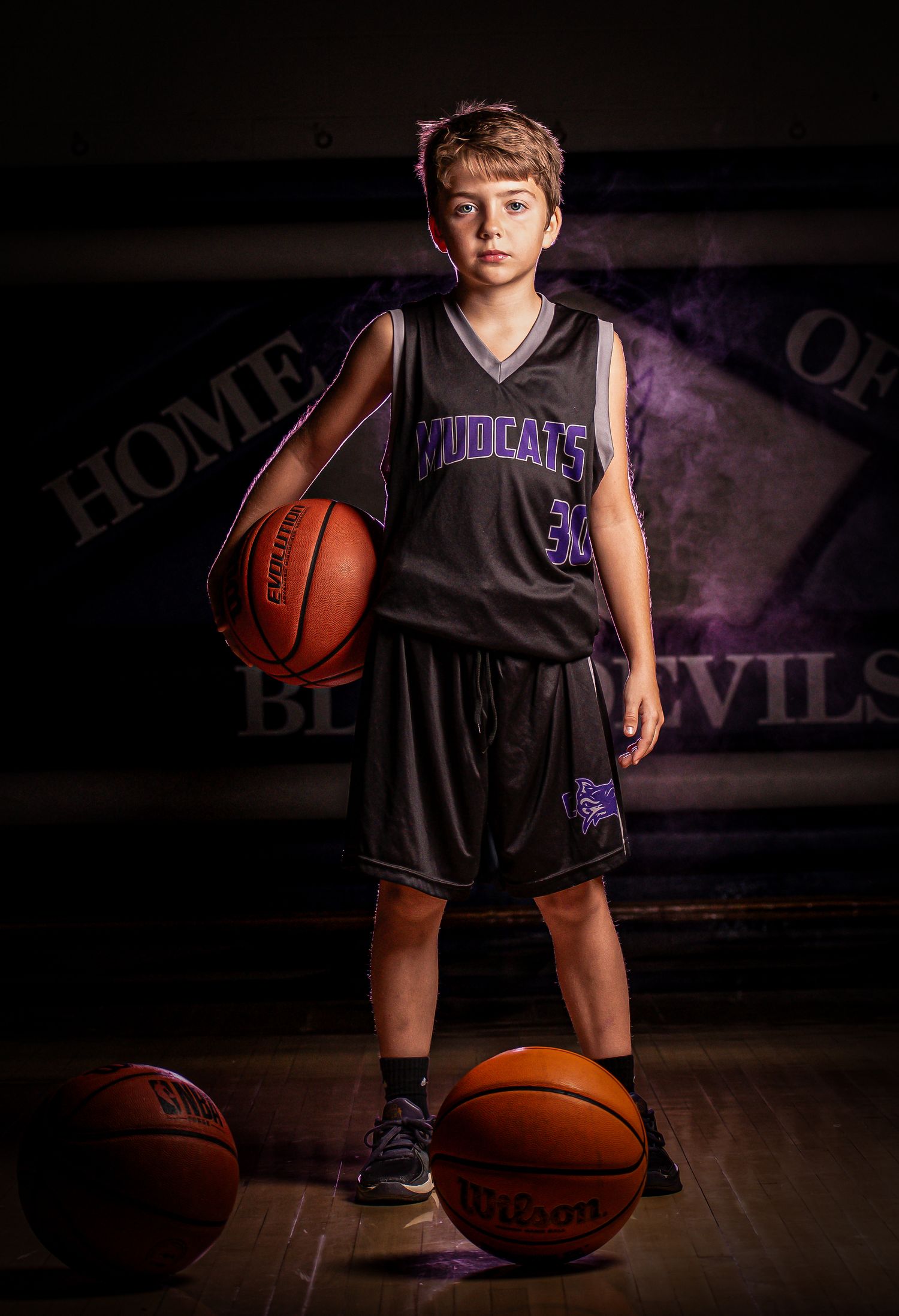 Basketball player in Wildcats uniform poses with multiple basketballs in dramatic studio lighting.