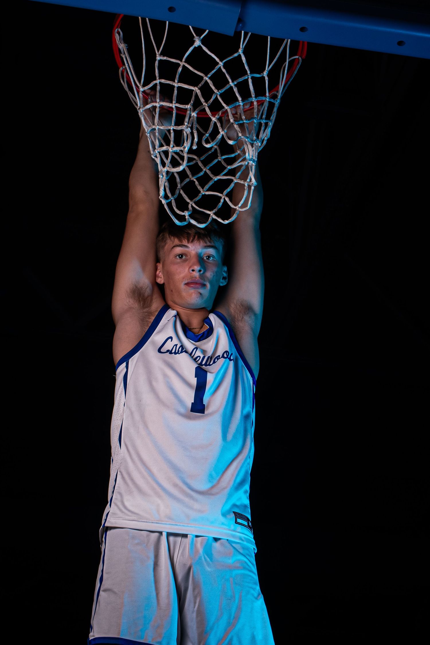 Basketball player touches net while wearing white Castlewood jersey number 1 in dark setting.