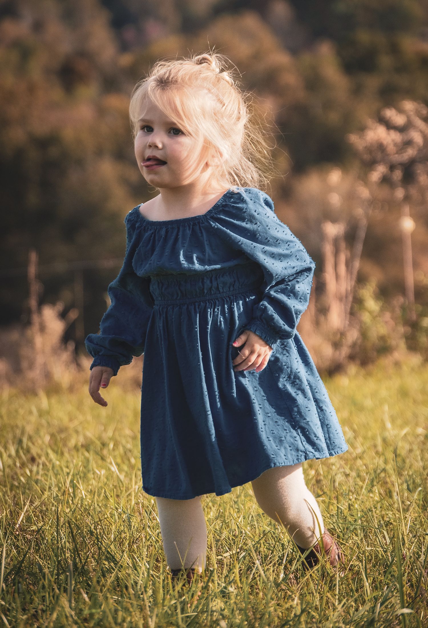 Playful movement captured as child in blue dress dances through meadow grass.