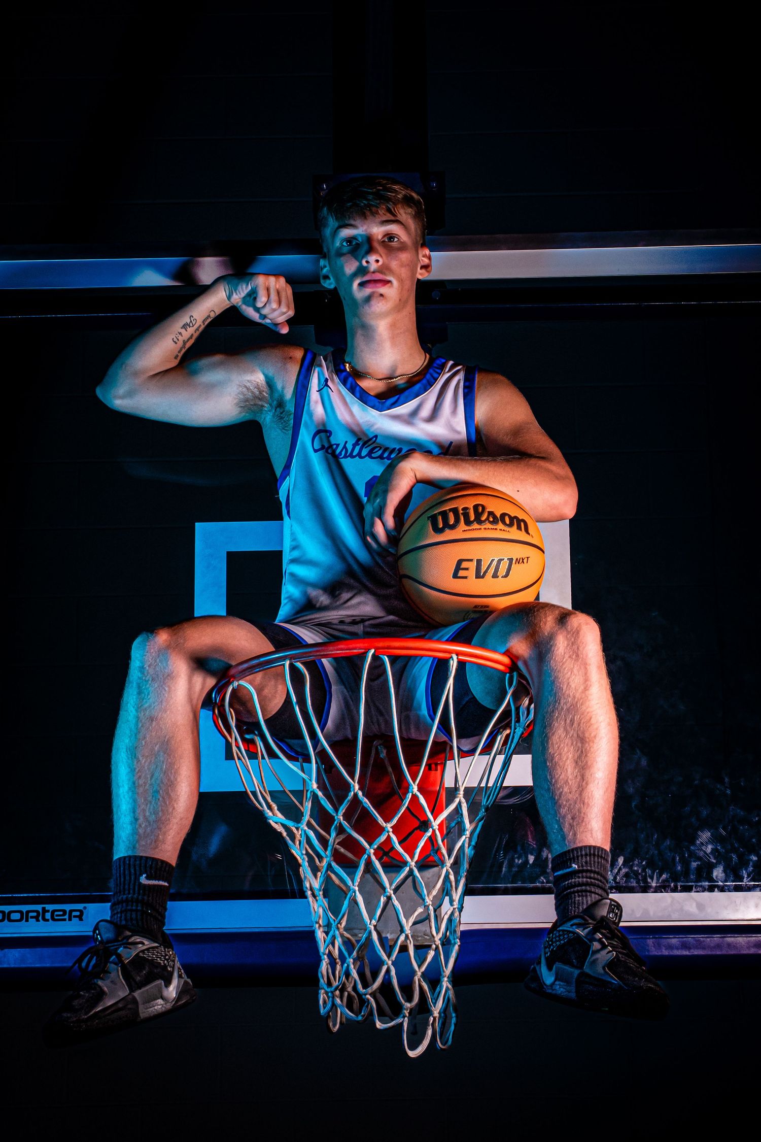 Player in Castlewood jersey poses on basketball hoop with Wilson ball in dramatic lighting.