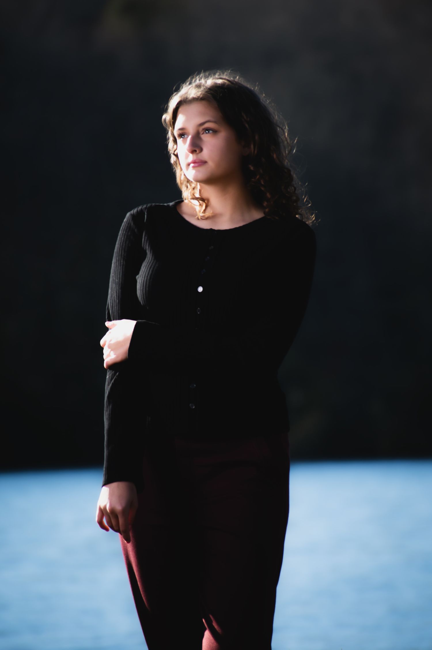 A figure in a black dress poses against a dark background with blue lighting creating a dramatic silhouette effect.