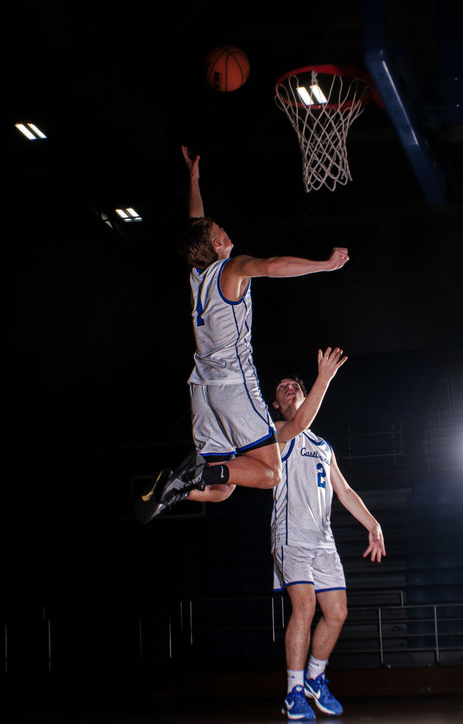 Basketball players execute coordinated jumping play near hoop.