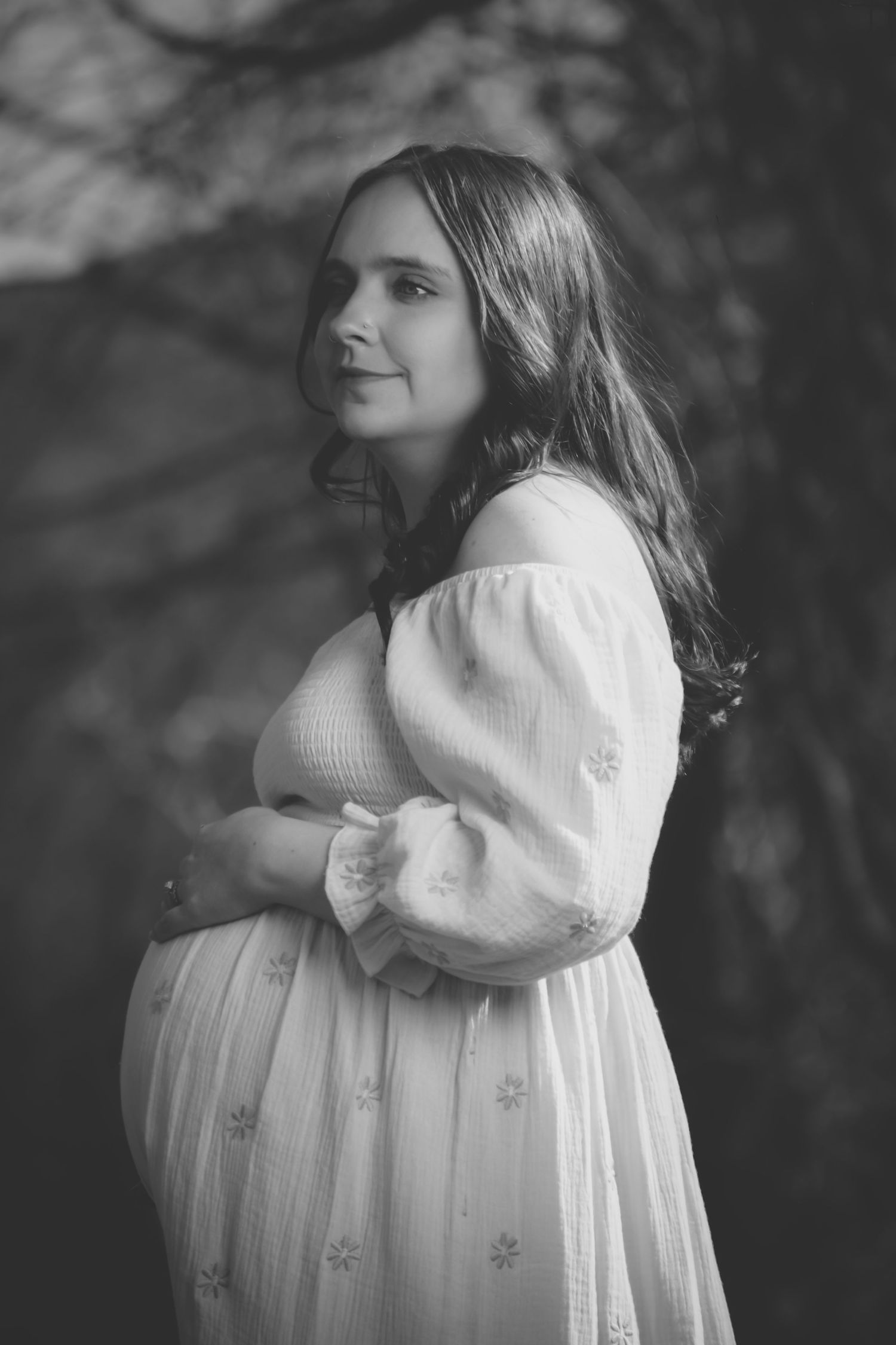 Black and white portrait of an expectant mother in a flowing white dress with puff sleeves looking to the side.